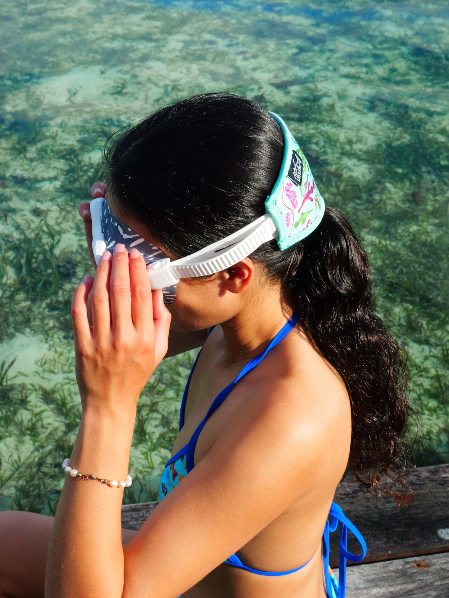 Dark haired woman seen from the side clear blue water seahorse design with green background neoprene mask strap tamer fitted to mask ocean illustration by Diver Mon Art