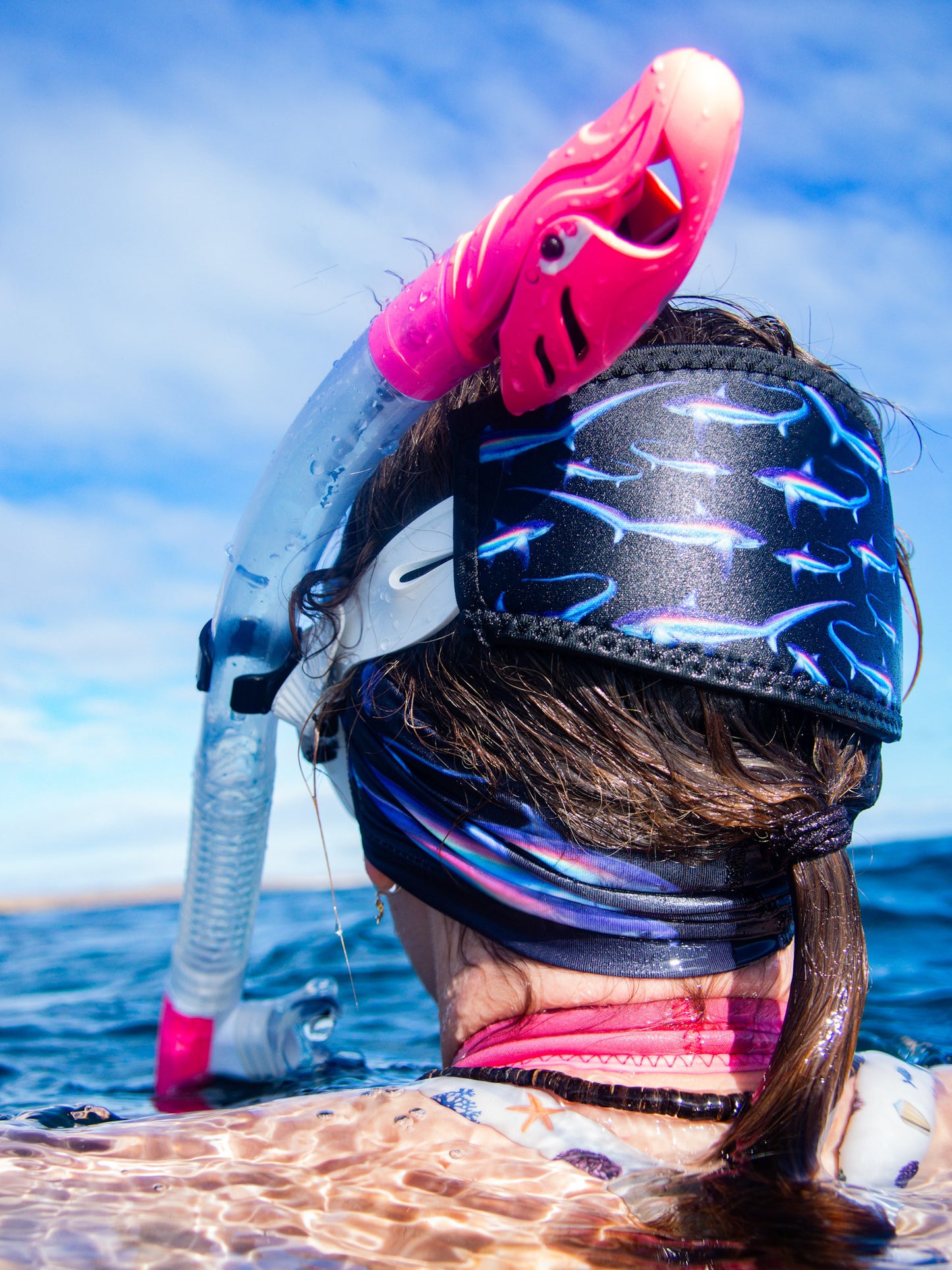 Dark haired woman seen above clear blue water wearing the limited addition black thresher UV gaiter buff made from recycled polyester-spandex matching with the black neoprene mask tamer ocean illustration by Diver Mon Art