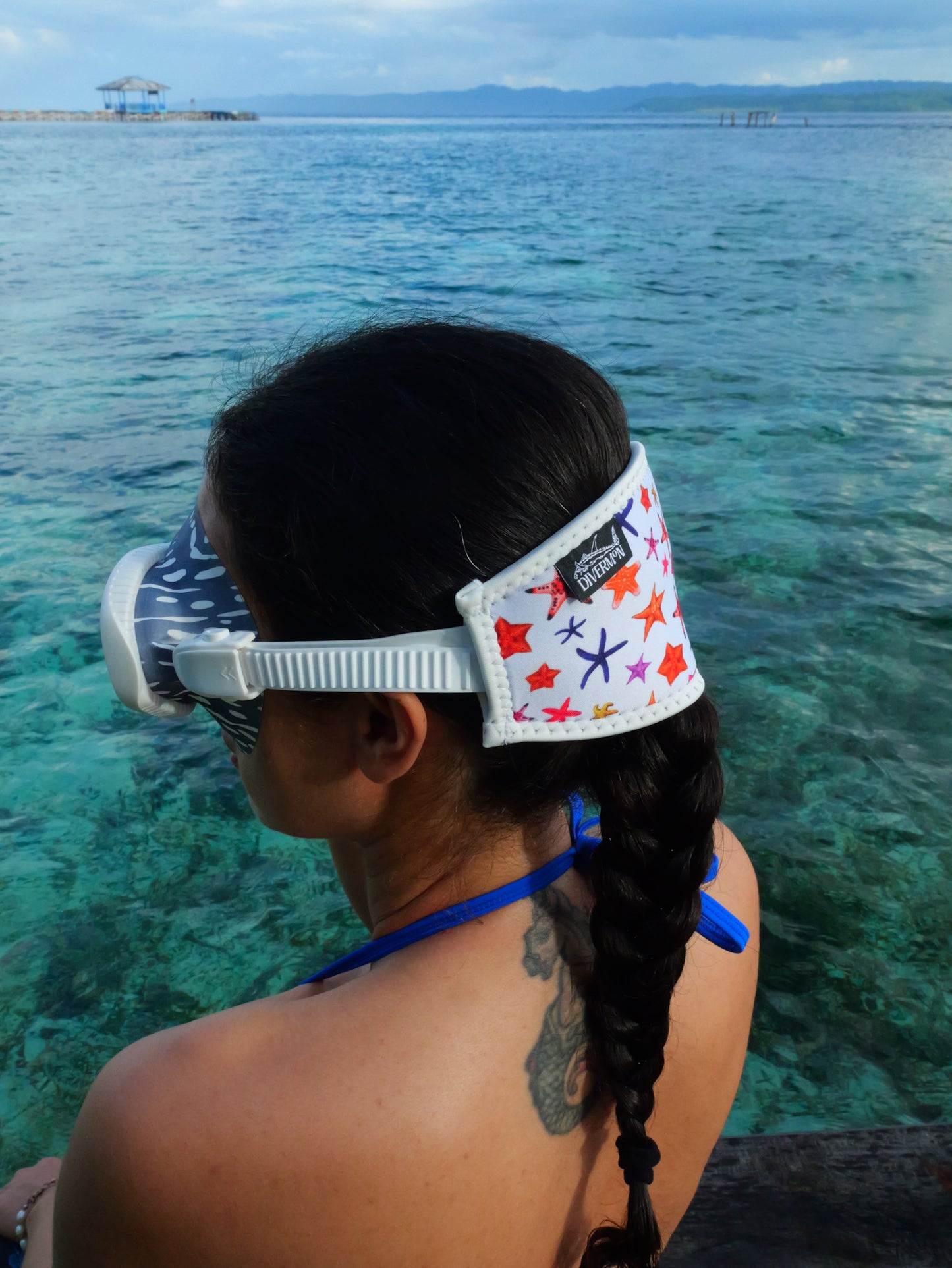 Dark haired woman shown from side view in blue clear water close up white sea star design neoprene mask strap tamer fitted to a mask ocean illustration by Diver Mon Art