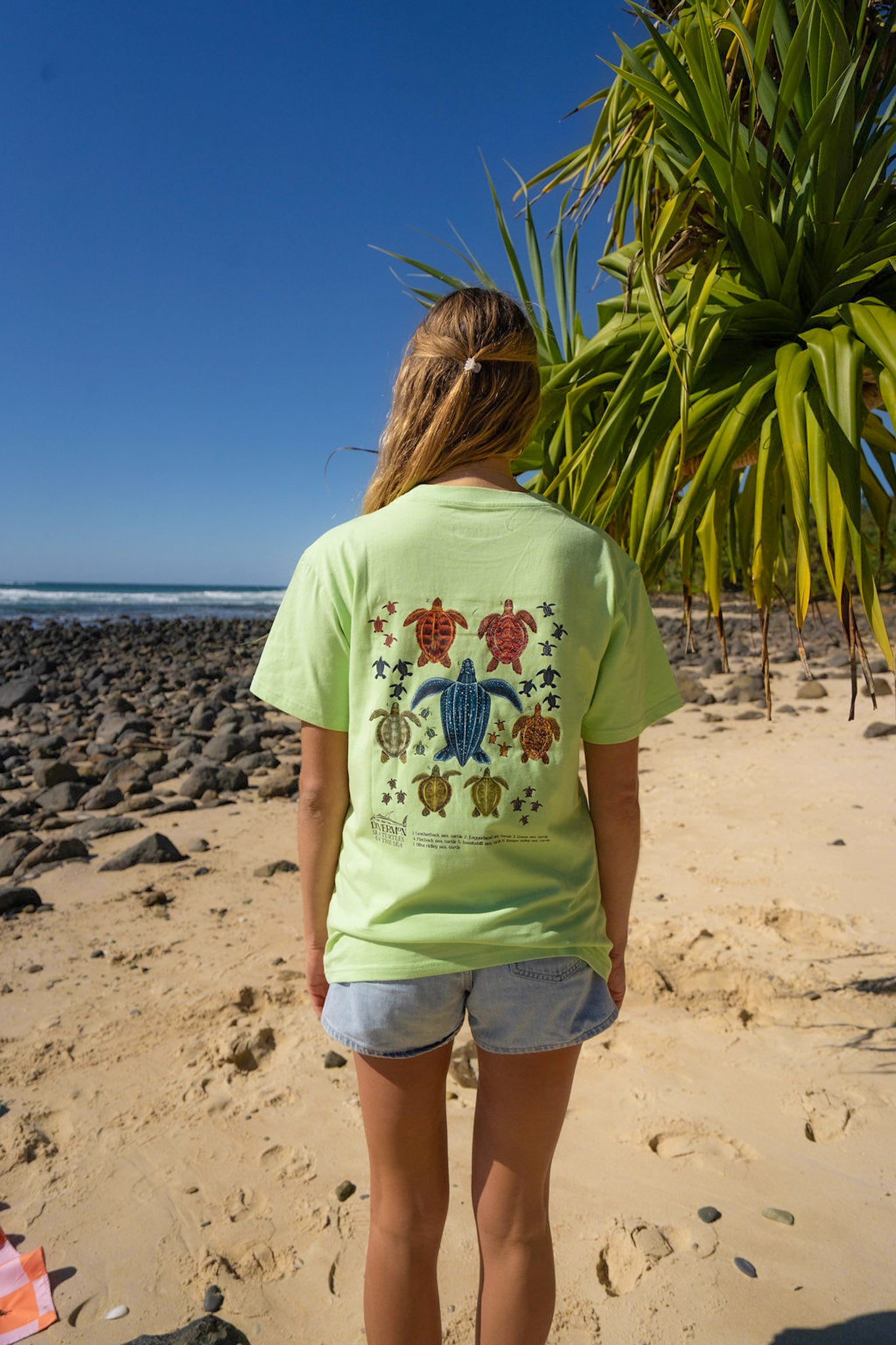 Person wearing a light green t-shirt with Diver Mon Art turtle design on a beach
