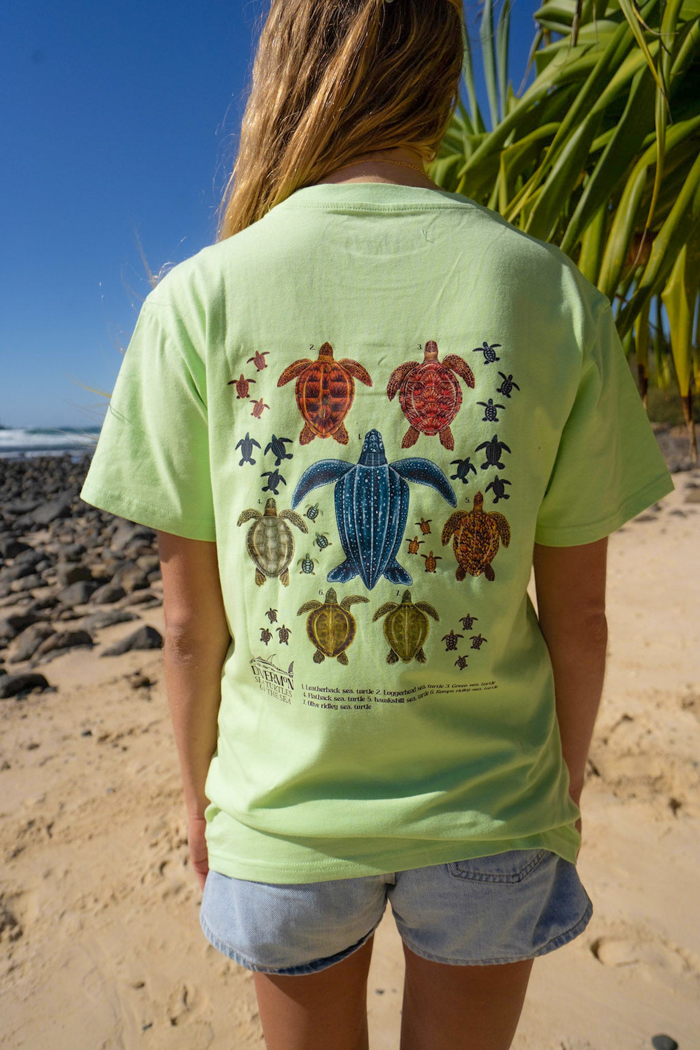 Person wearing a light green t-shirt with turtle design by Diver Mon Art on a beach