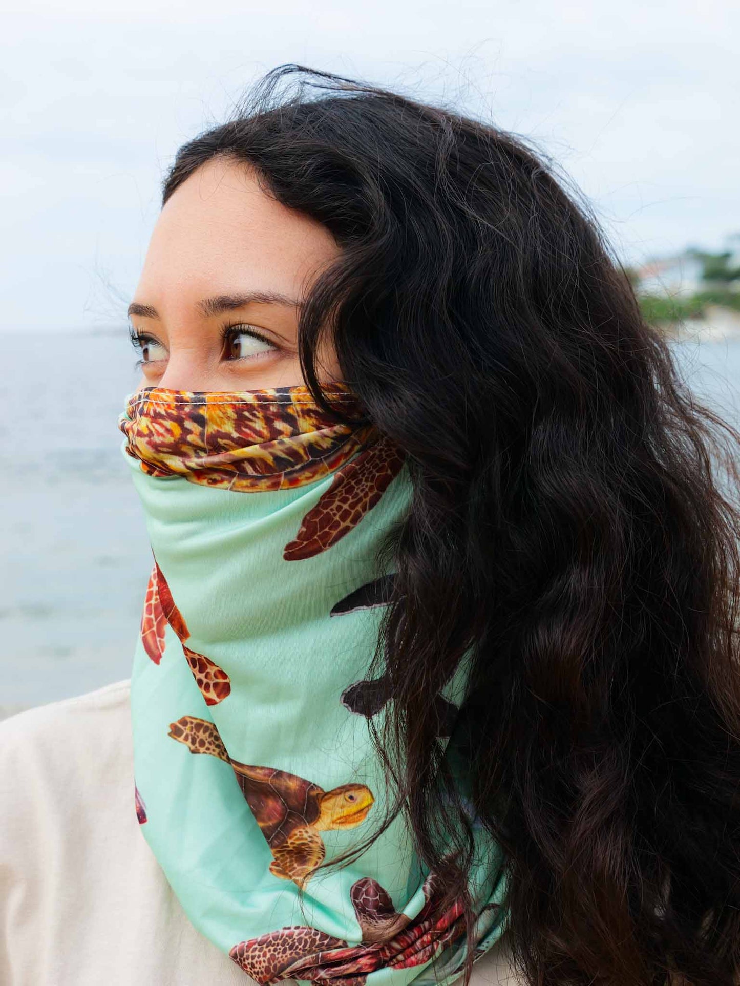 Dark haired women shown side view at the beach wearing the big turtles green UV gaiter buff made from recycled polyester-spandex around bottom half of face neck ocean illustration by Diver Mon Art 