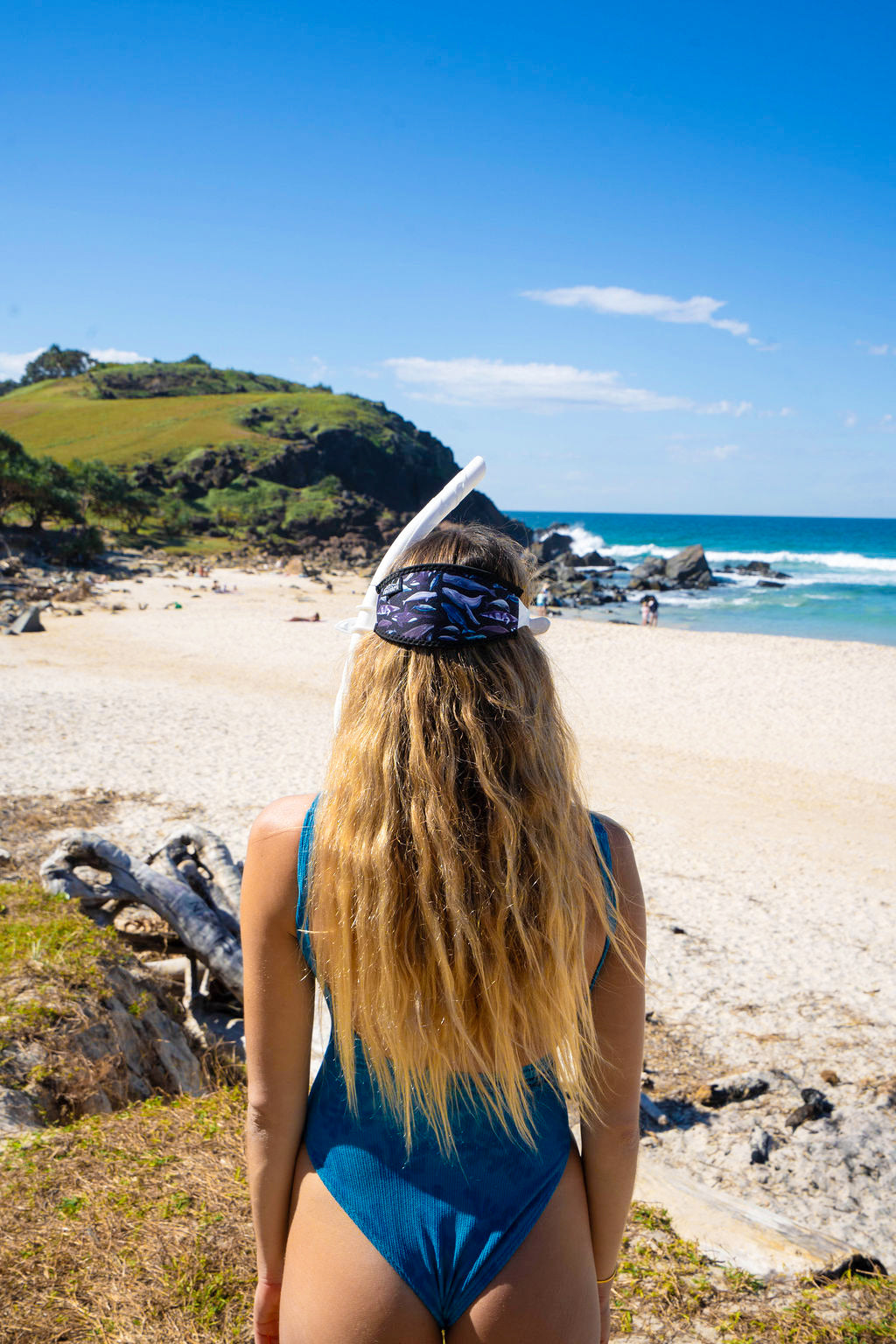 Blonde haired woman seen from behind at the beach with the Dolphins, whales and porpoises with a black background neoprene mask strap tamer ocean illustration by Diver Mon Art 
