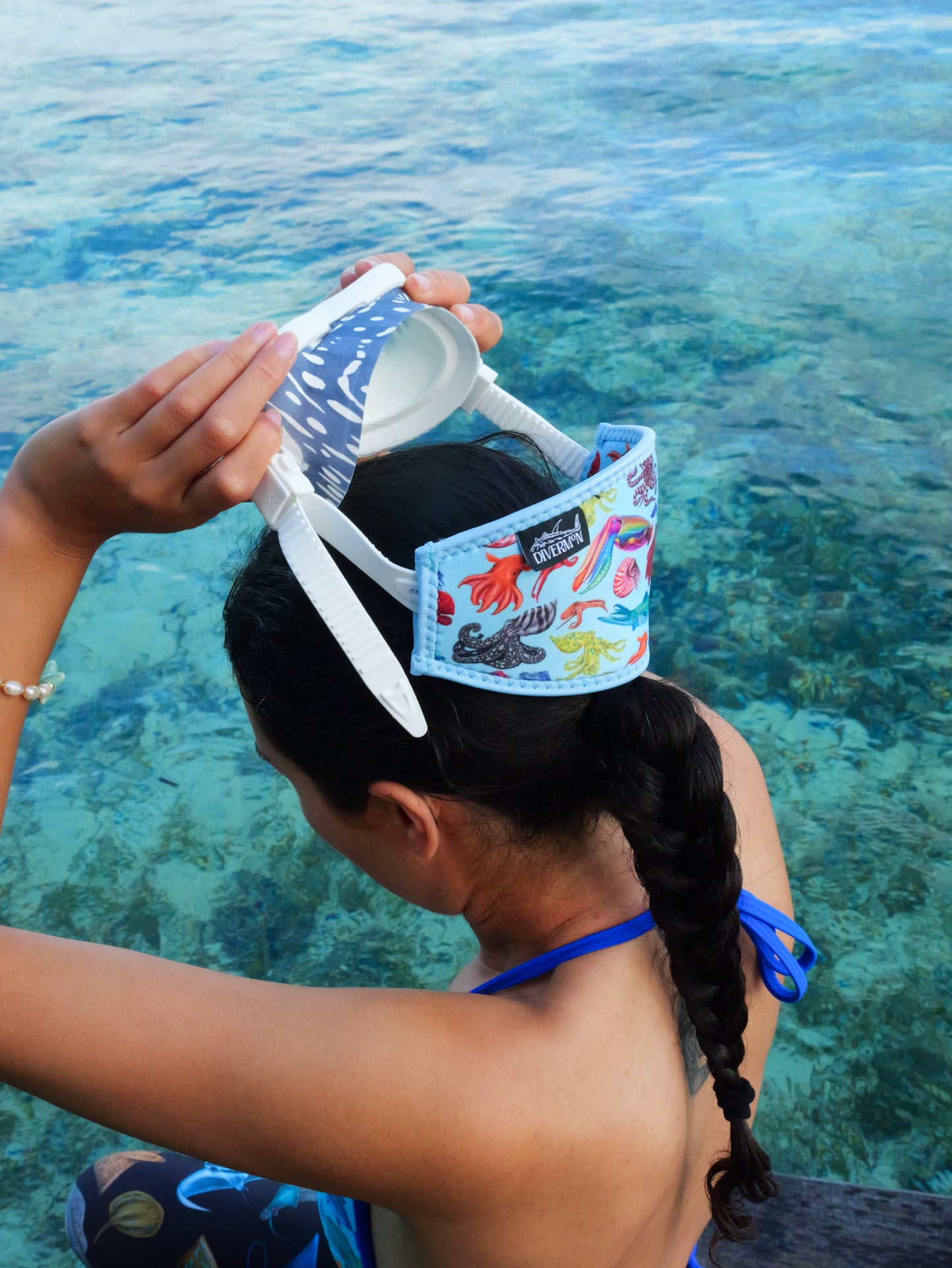 Dark haired woman taking off mask in clear blue water cephalopod with a light blue background neoprene mask strap tamer ocean illustration by Diver Mon Art 
