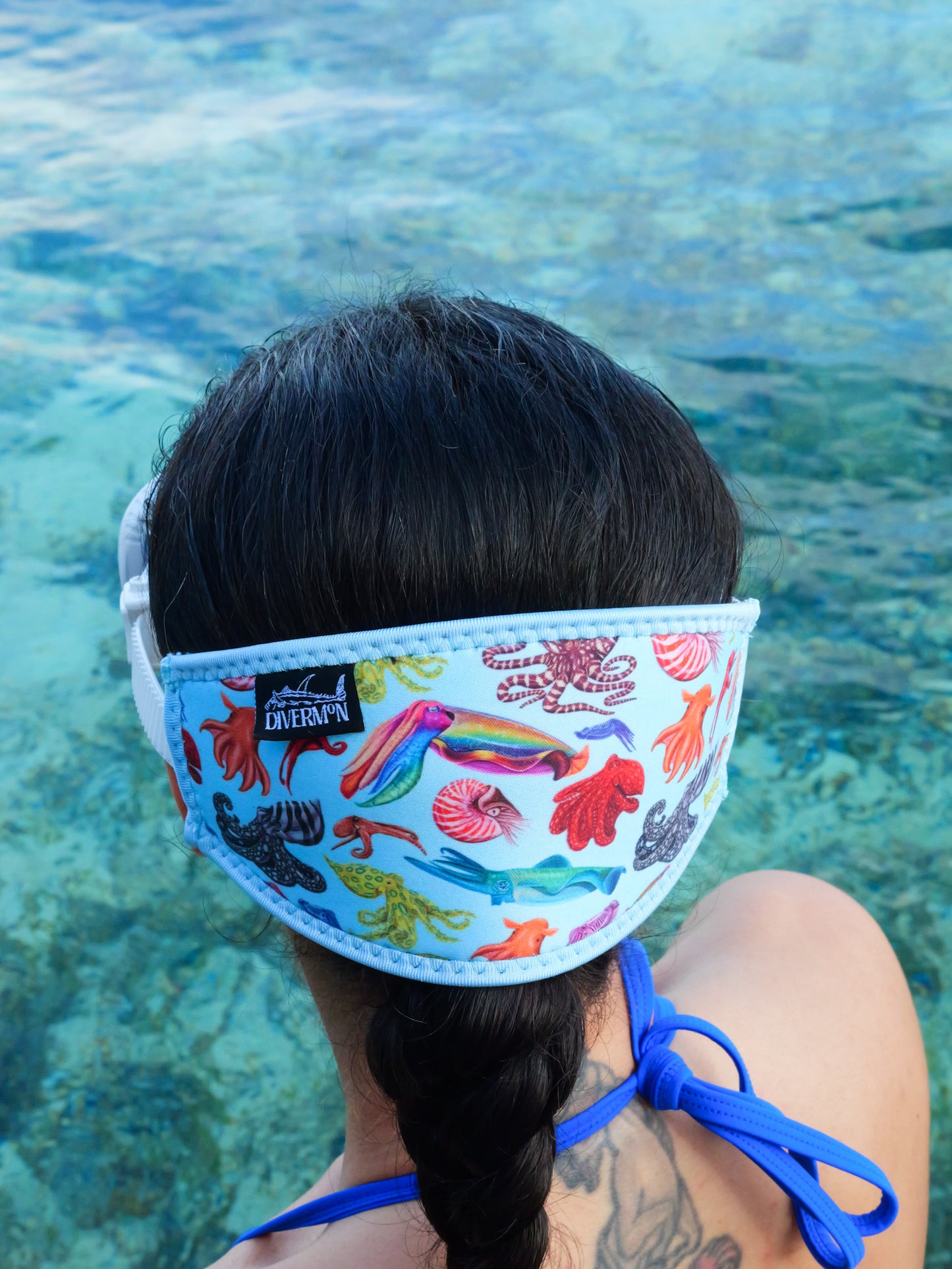 Dark haired woman seen from behind in clear blue water cephalopod with a light blue background neoprene mask strap tamer ocean illustration by Diver Mon Art 
