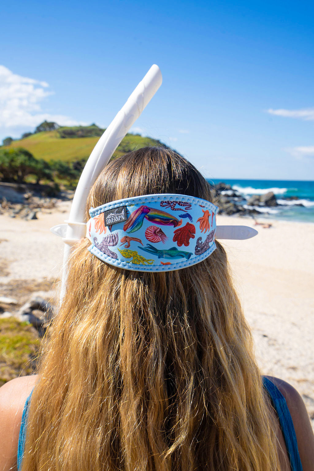 Blonde haired woman seen close up from behind at the beach with the cephalopod light blue background neoprene mask strap tamer ocean illustration by Diver Mon Art 
