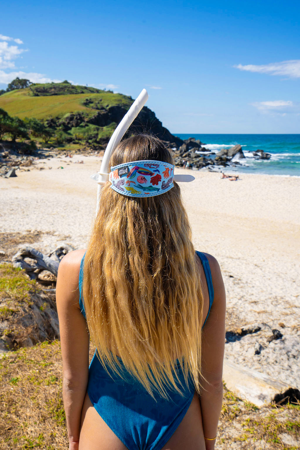 Blonde haired woman seen from behind at the beach with the cephalopod light blue background neoprene mask strap tamer ocean illustration by Diver Mon Art 