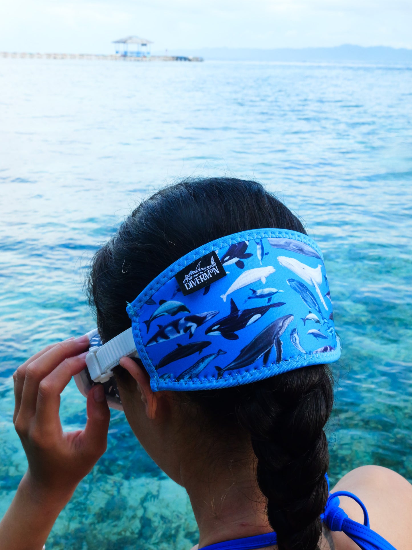 Dark haired woman shown from behind in blue clear water close up with the Dolphins, whales and porpoises with a light blue background neoprene mask strap tamer ocean illustration by Diver Mon Art  