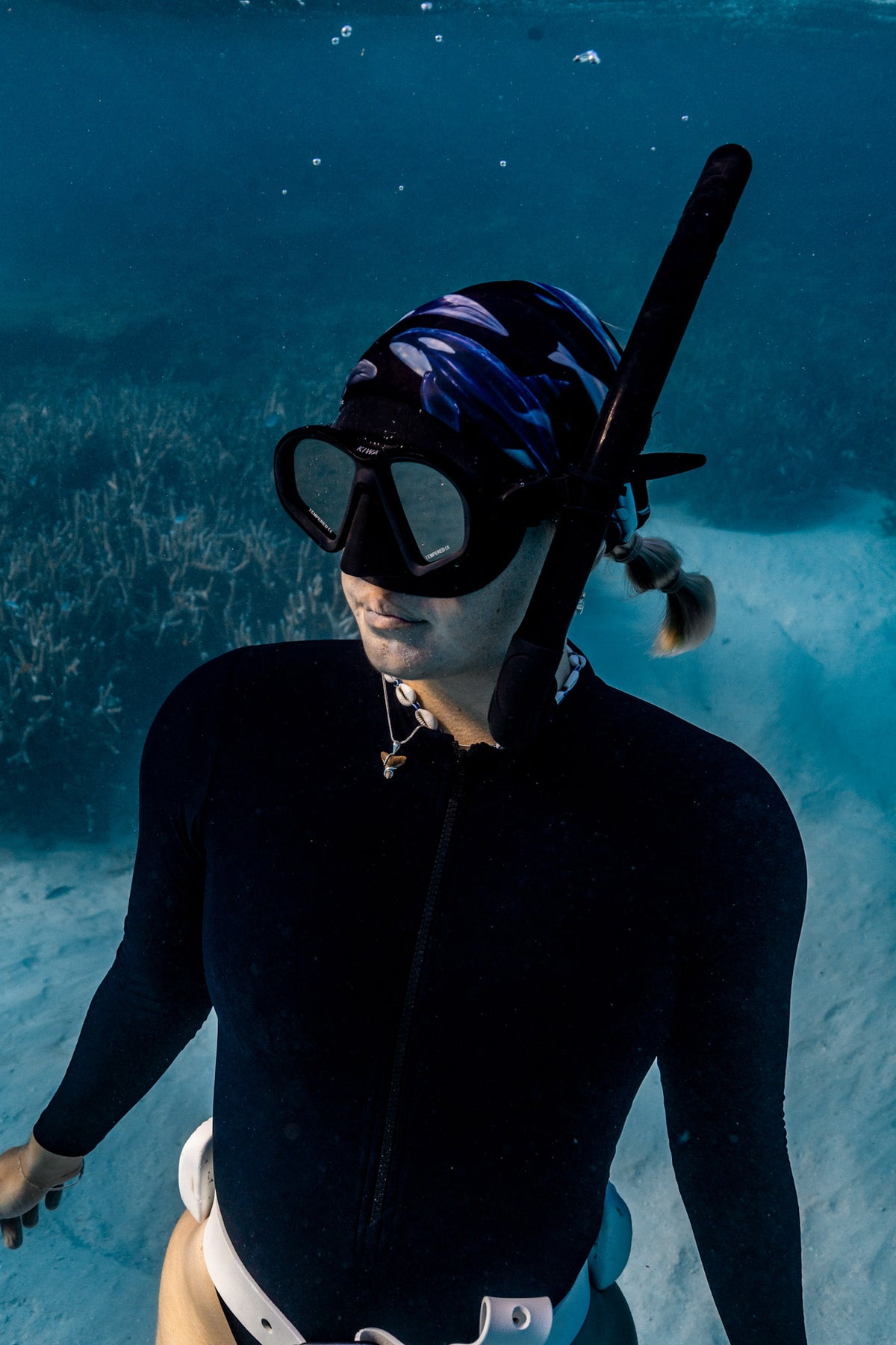 Blonde haired women shown close up great detail underwater clear blue water wearing cetaceans black UV gaiter buff design made from recycled polyester-spandex ocean illustration by Diver Mon Art