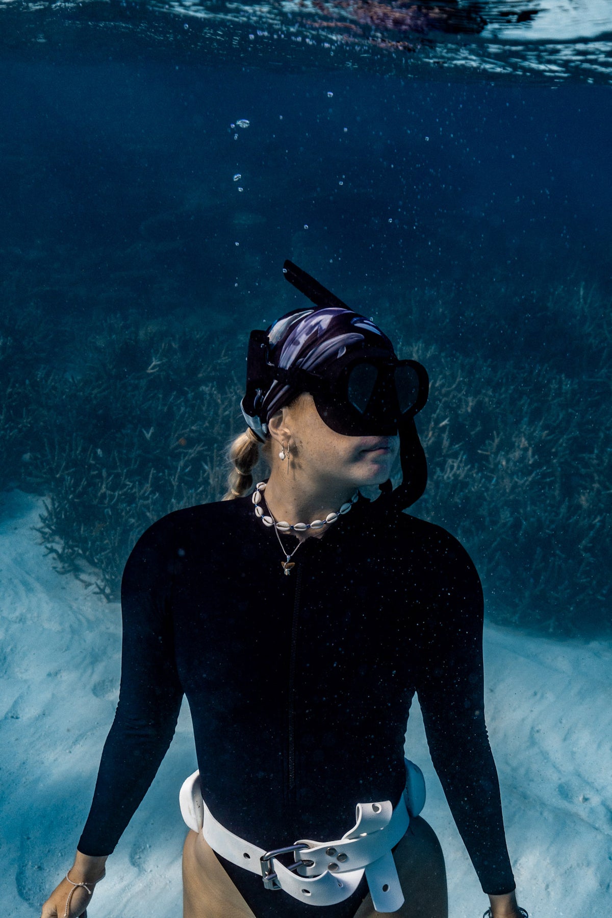 Blonde haired women shown underwater clear blue water wearing cetaceans black UV gaiter buff design made from recycled polyester-spandex ocean illustration by Diver Mon Art