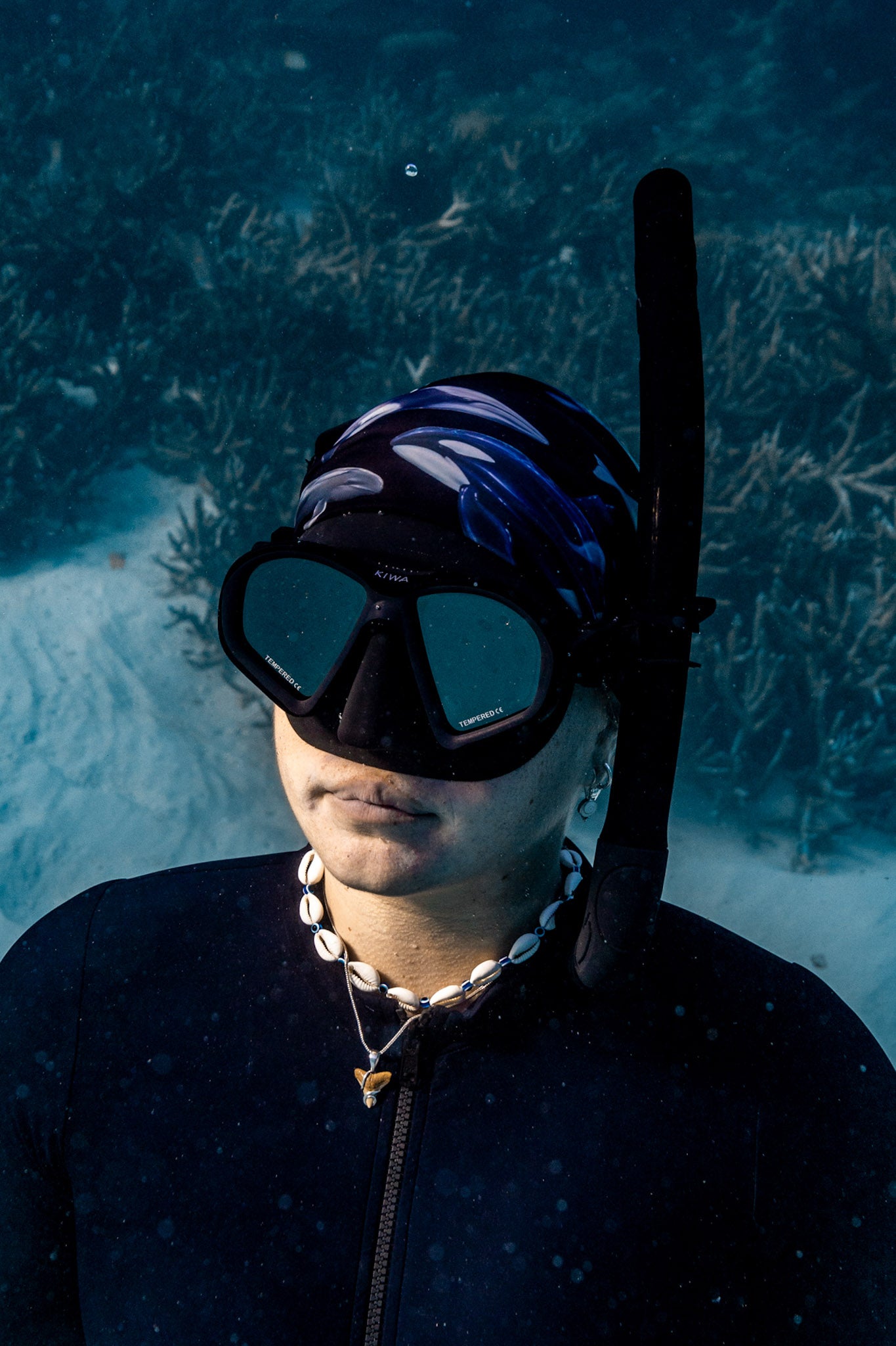 Blonde haired women shown close up great detail underwater clear blue water wearing cetaceans black UV gaiter buff design made from recycled polyester-spandex ocean illustration by Diver Mon Art