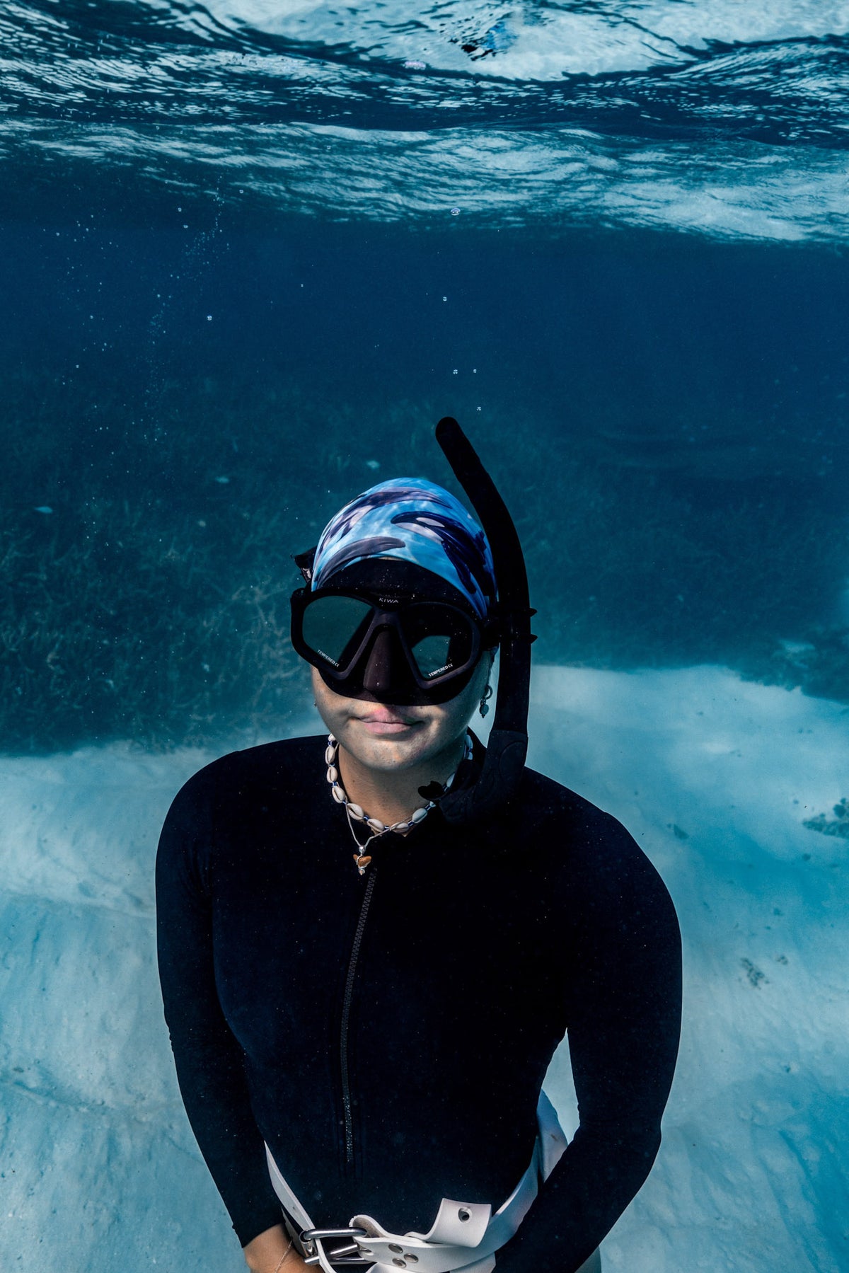 Blonde haired women shown underwater clear blue water wearing cetaceans blue UV gaiter buff design made from recycled polyester-spandex ocean illustration by Diver Mon Art