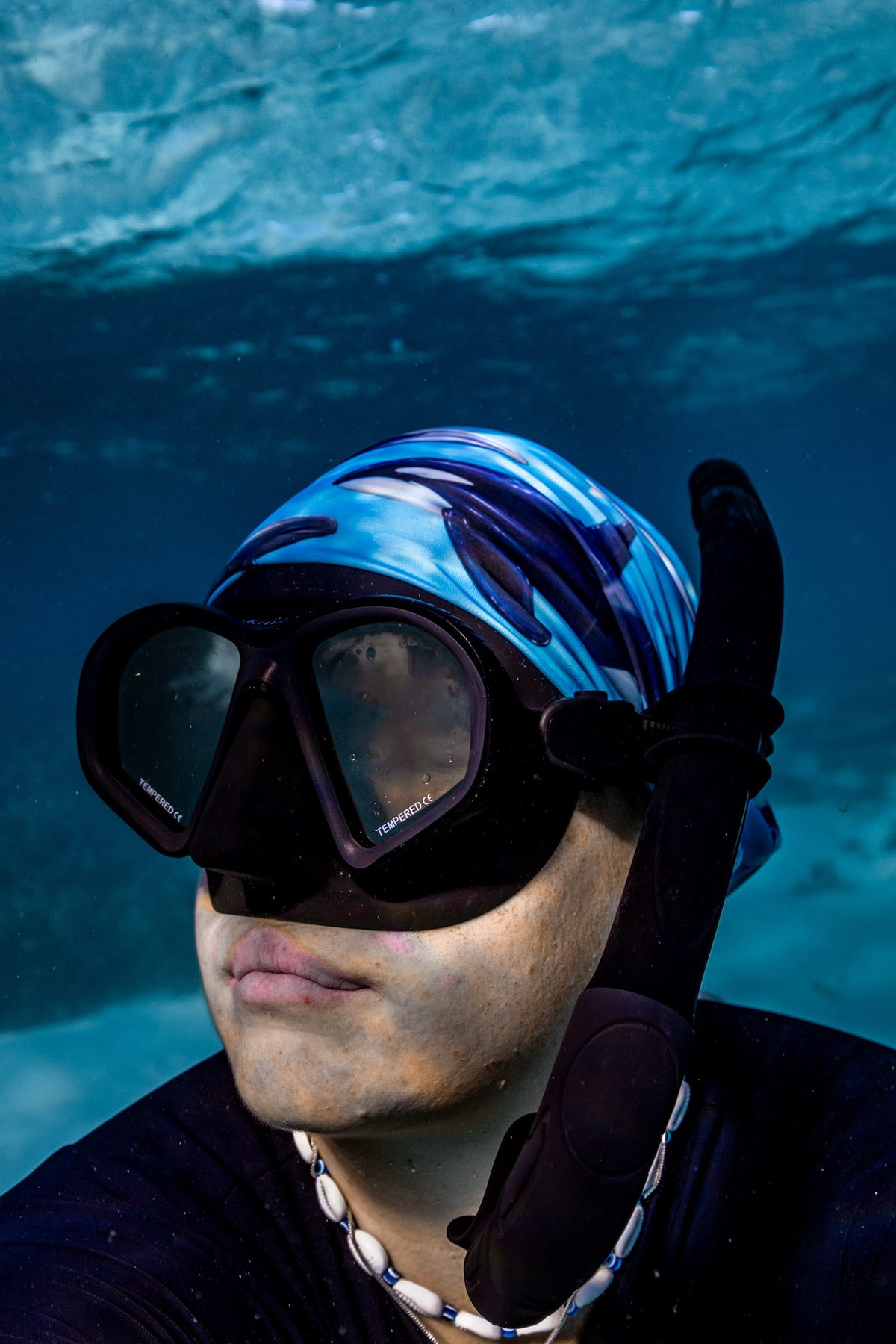 Blonde haired women shown close up great detail underwater clear blue water wearing cetaceans blue  UV gaiter buff design made from recycled polyester-spandex ocean illustration by Diver Mon Art