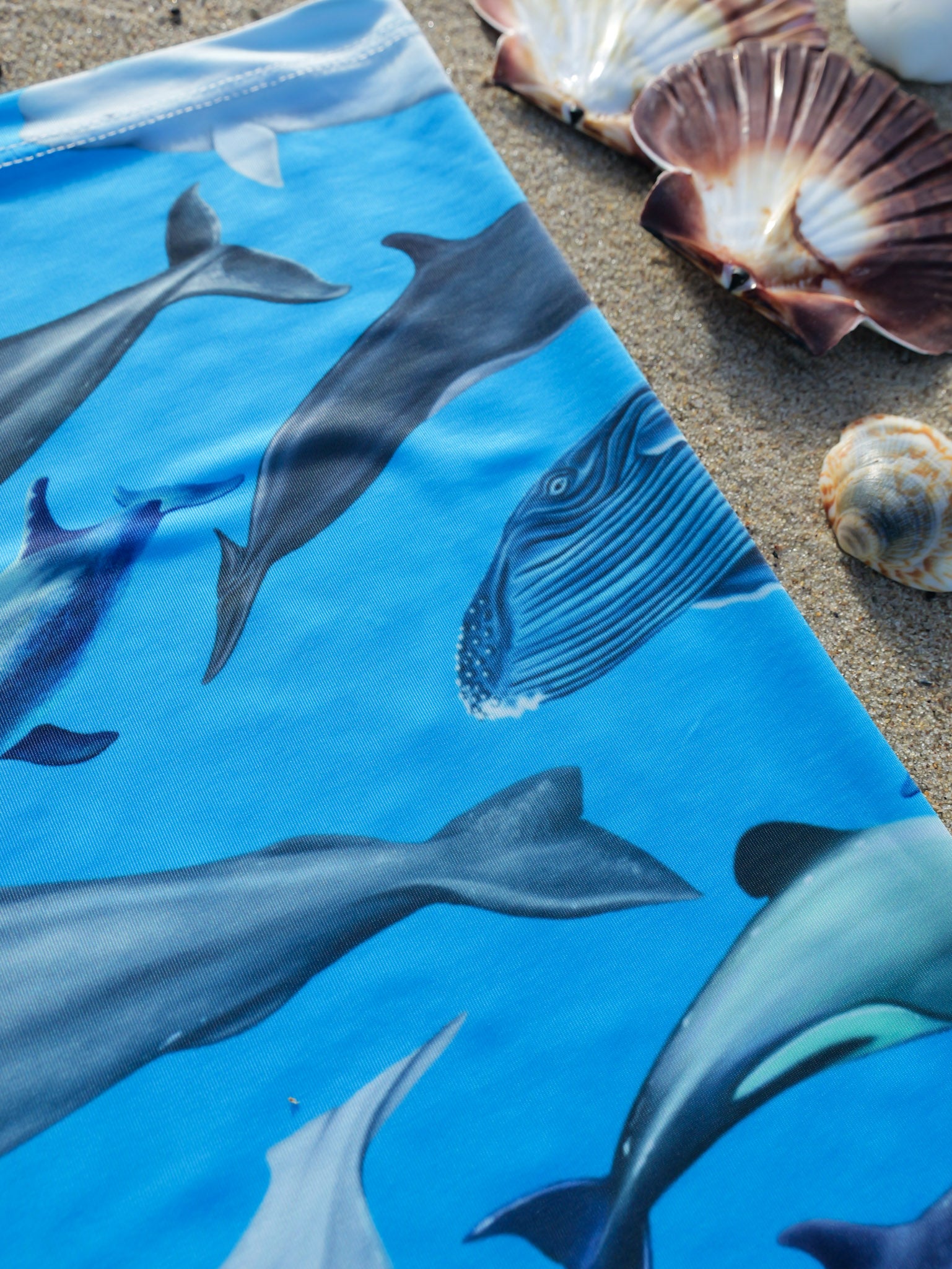 Cetaceans blue UV gaiter buff design shown close up in great detail sand background made from recycled polyester-spandex ocean illustration by Diver Mon Art 