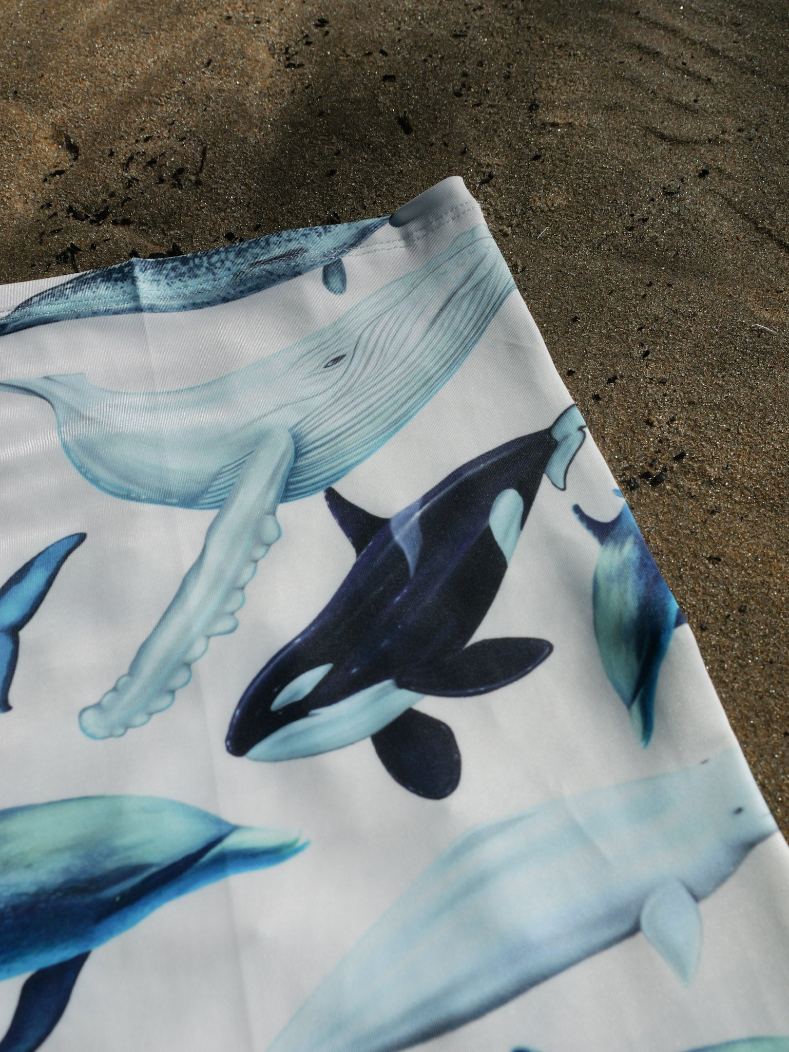 Cetaceans white UV gaiter buff design shown top right corner close up in great detail sand background made from recycled polyester-spandex ocean illustration by Diver Mon Art 