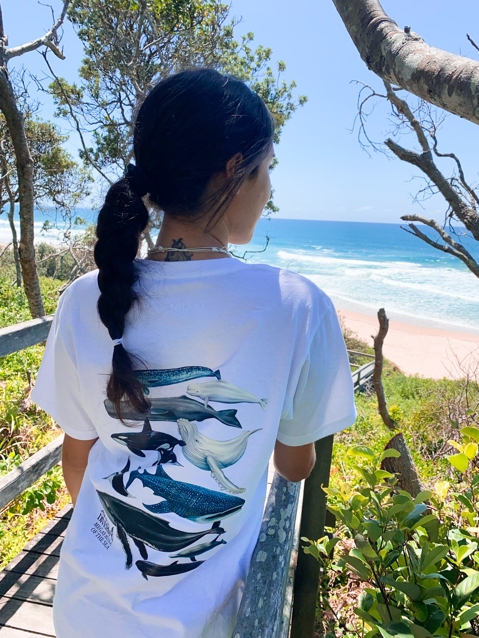 Person wearing a white t-shirt with whale designs by the ocean