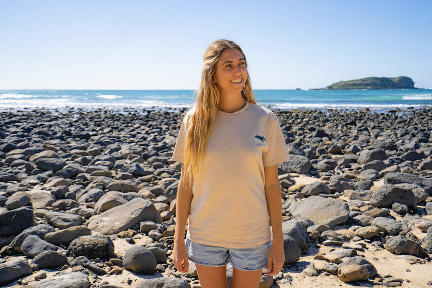 Woman standing on a rocky beach with ocean and sky in the background Diver Mon Art
