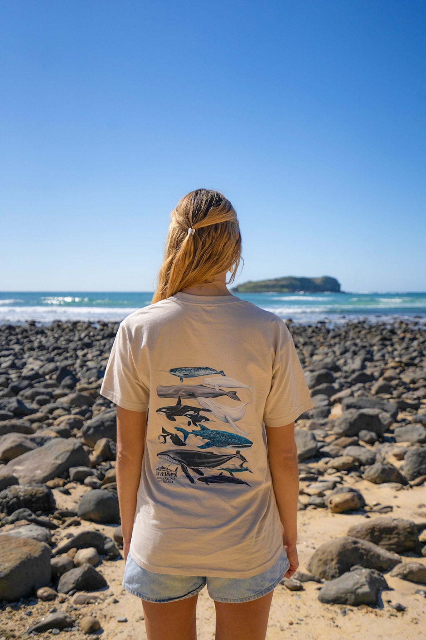 Woman wearing a Diver Mon Art t-shirt with whale design on a rocky beach