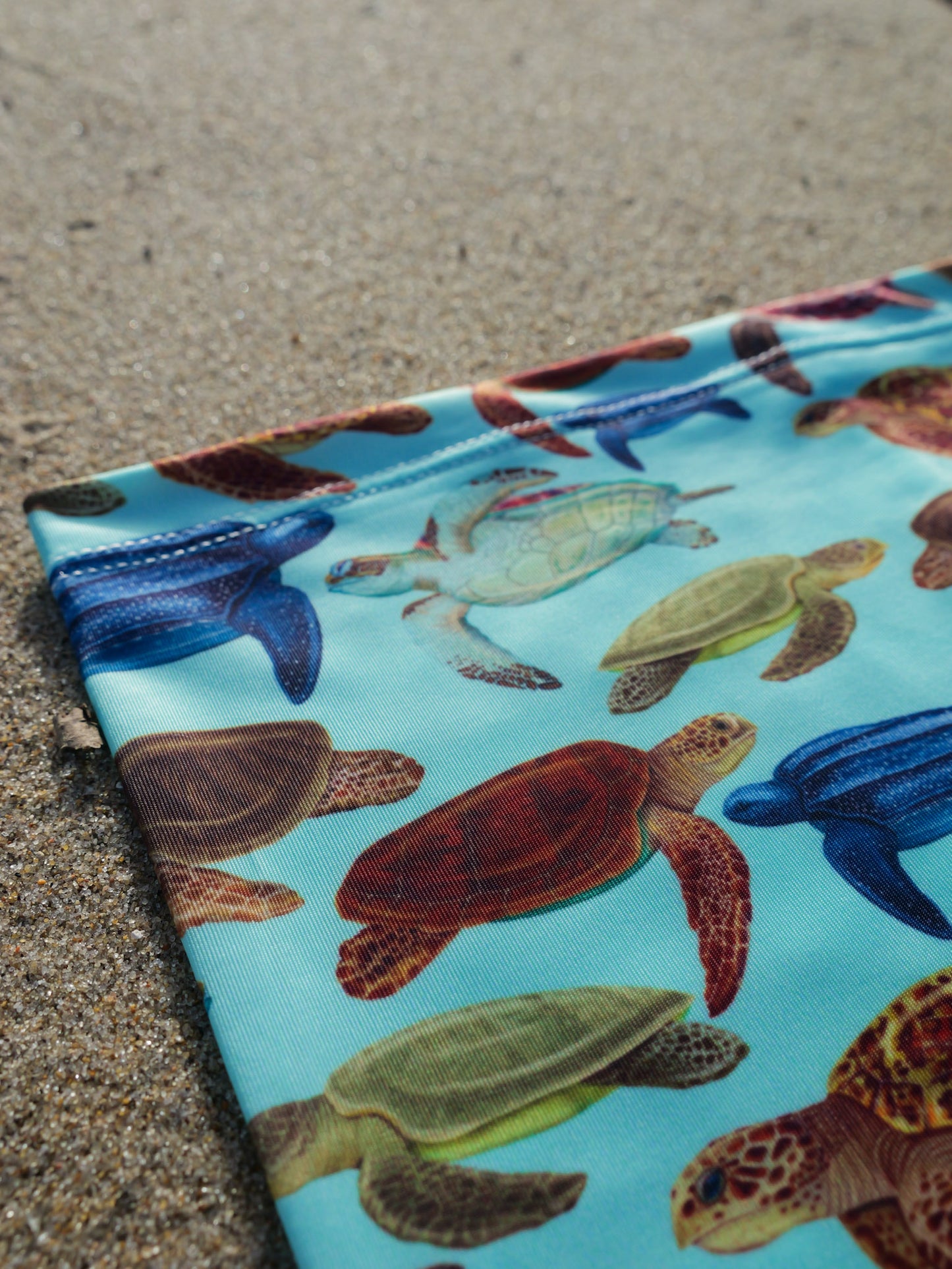 Mini turtles green UV gaiter buff design shown top left close up in great detail sand background made from recycled polyester-spandex ocean illustration by Diver Mon Art