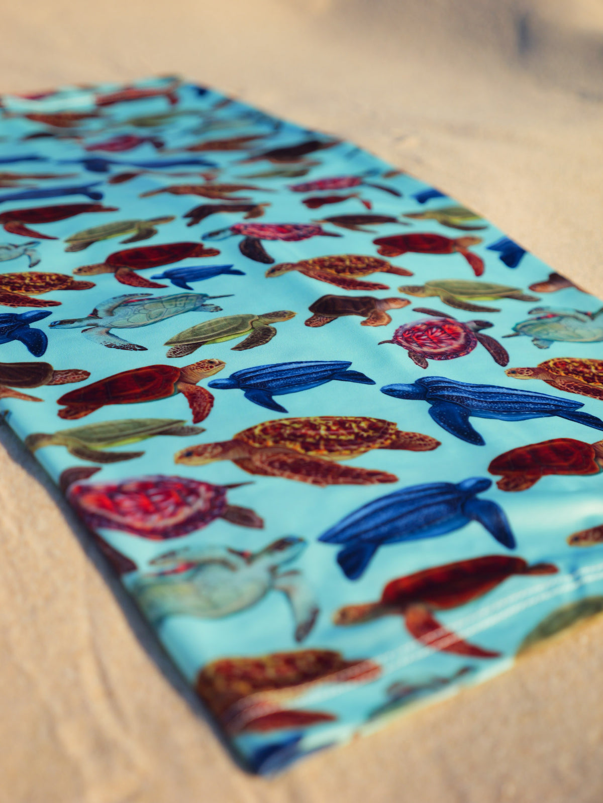 Mini turtles green UV gaiter buff design shown bottom left corner close up in great detail sand background made from recycled polyester-spandex ocean illustration by Diver Mon Art