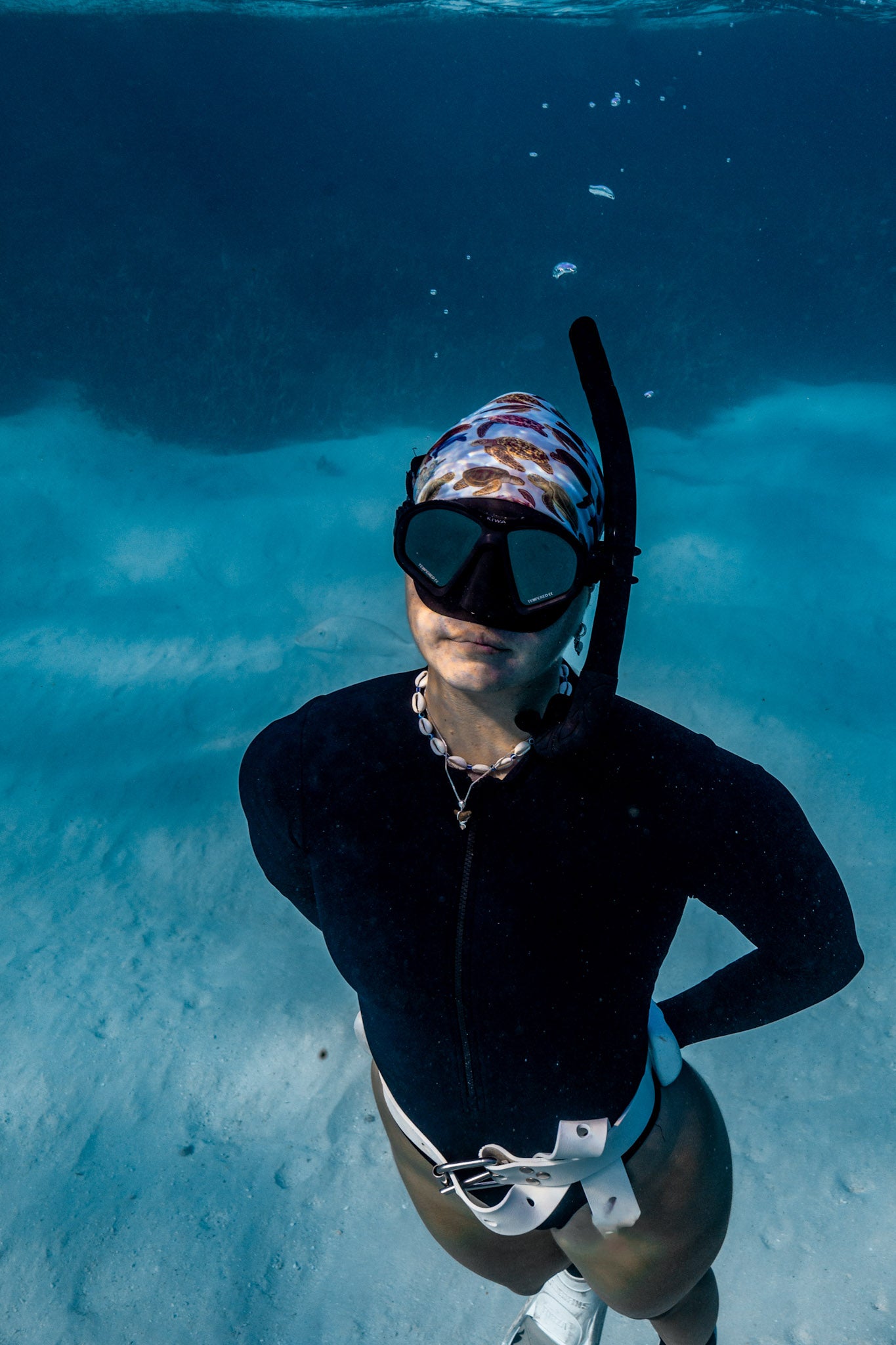 Blonde haired women shown underwater clear blue water wearing mini turtles green UV gaiter buff design made from recycled polyester-spandex ocean illustration by Diver Mon Art