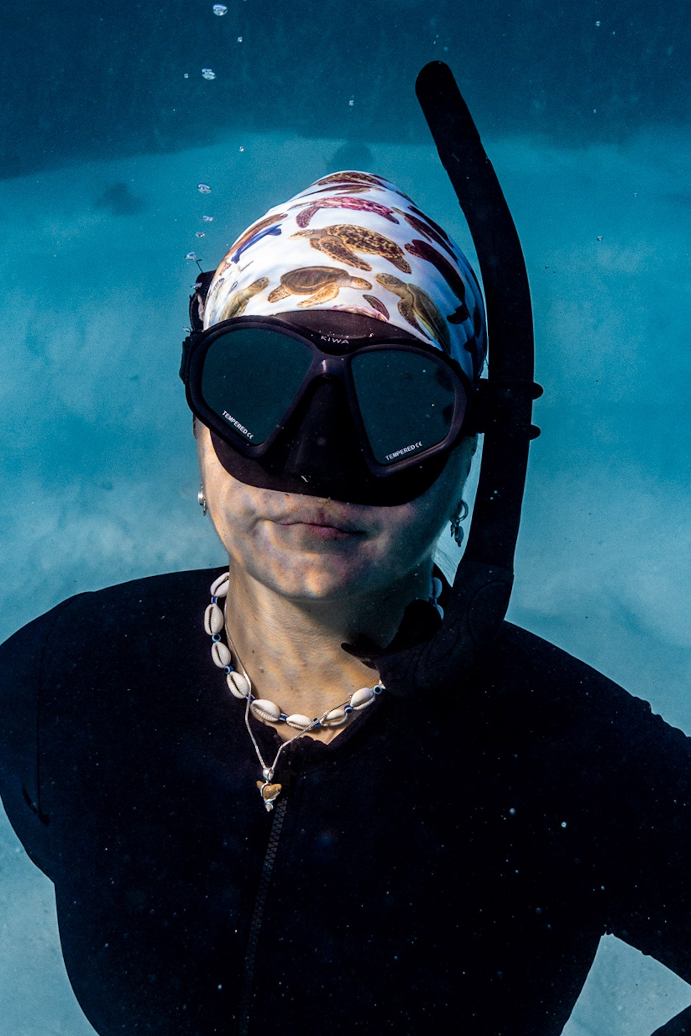 Blonde haired women shown close up great detail underwater clear blue water wearing mini turtles green UV gaiter buff design made from recycled polyester-spandex ocean illustration by Diver Mon Art