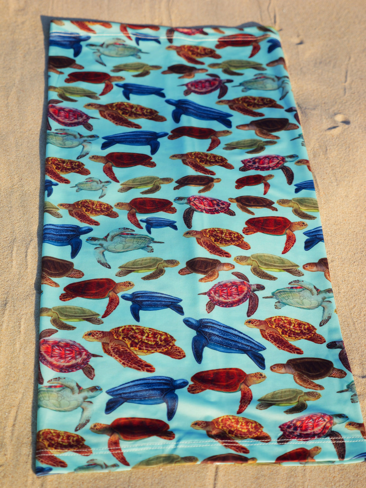 Mini turtles green UV gaiter buff design shown laid out close up in great detail sand background made from recycled polyester-spandex ocean illustration by Diver Mon Art