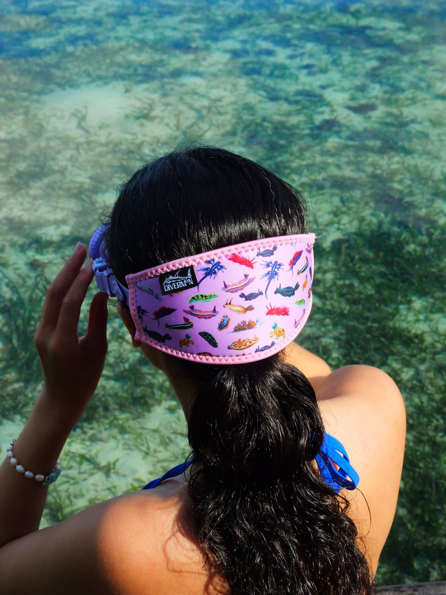 Dark haired woman shown from behind in blue clear water close up nudibranch pink design neoprene mask strap tamer ocean illustration by Diver Mon Art
