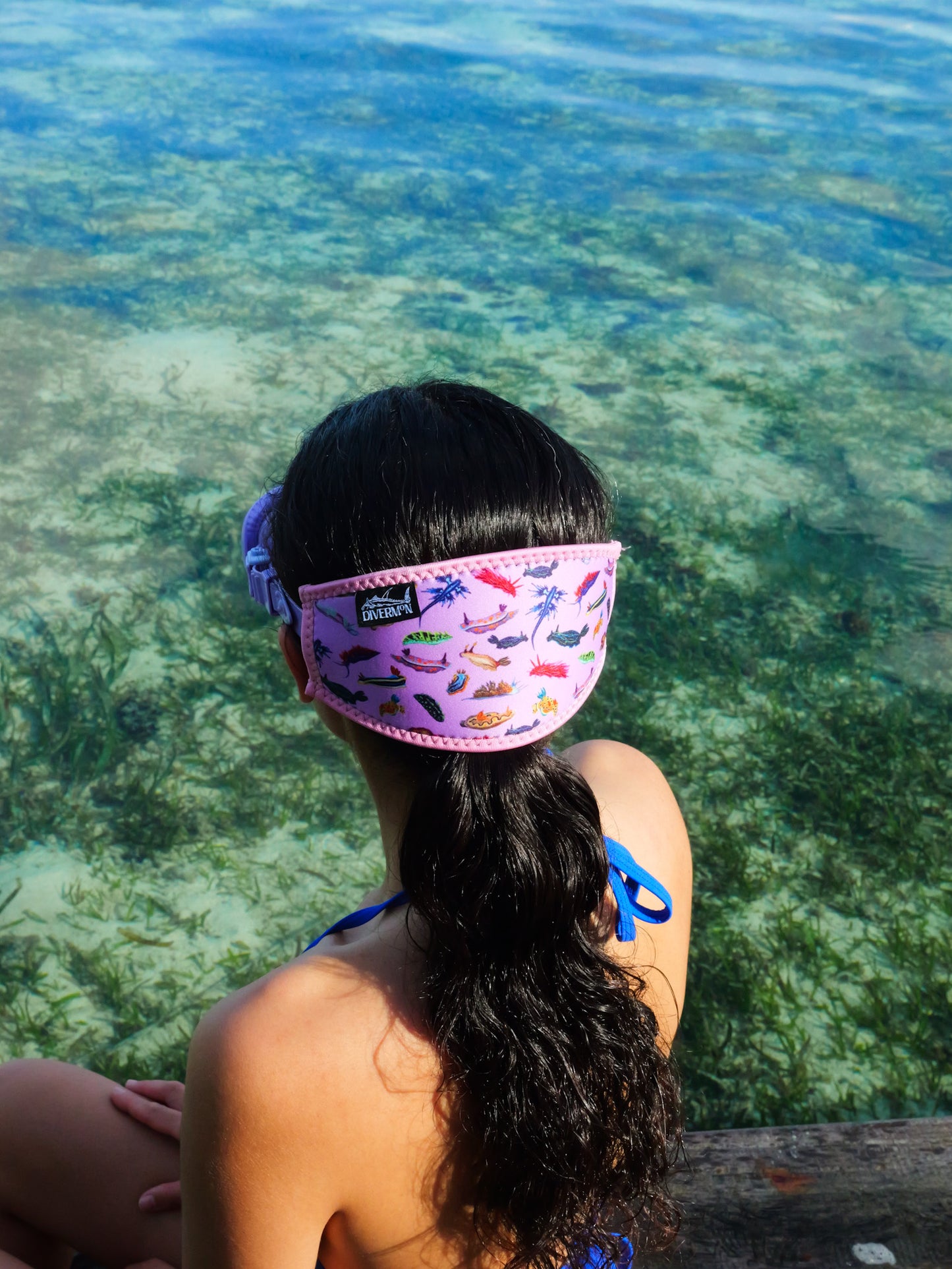 Dark haired woman shown from behind in blue clear water close up nudibranch pink design neoprene mask strap tamer ocean illustration by Diver Mon Art