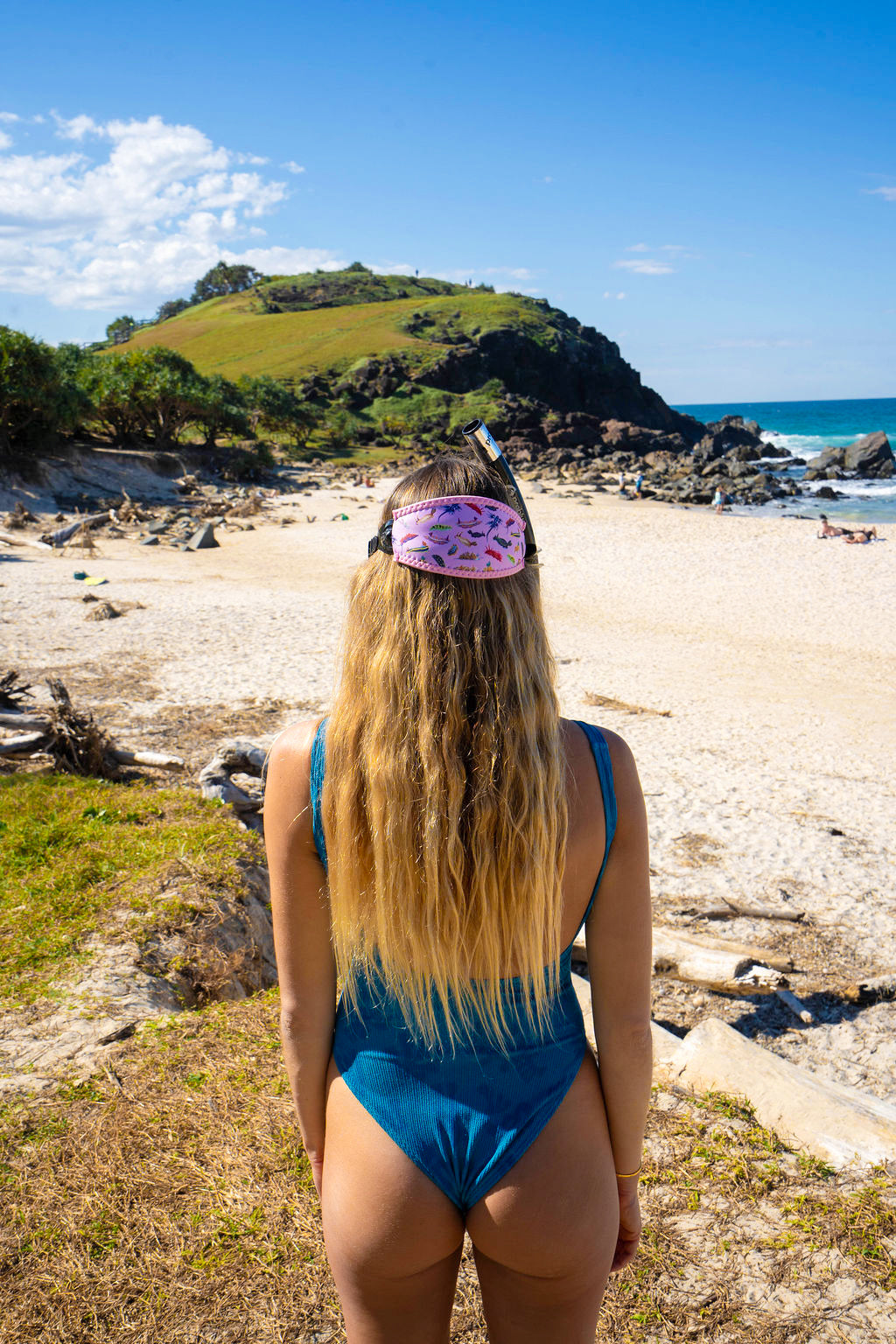 Blonde haired woman seen from behind at the beach with the nudibranch pink design neoprene mask strap tamer ocean illustration by Diver Mon Art