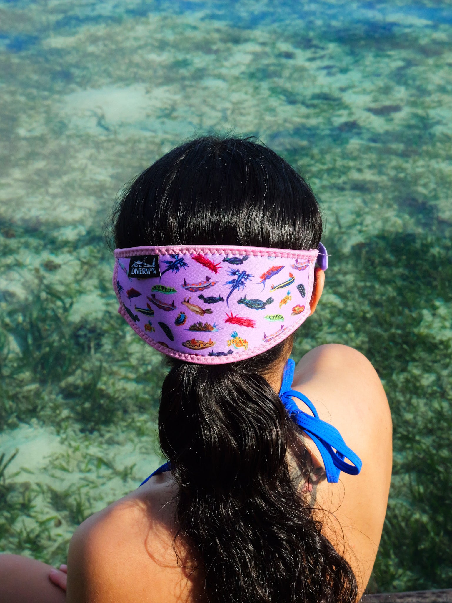 Dark haired woman shown from behind in blue clear water close up nudibranch pink design neoprene mask strap tamer ocean illustration by Diver Mon Art