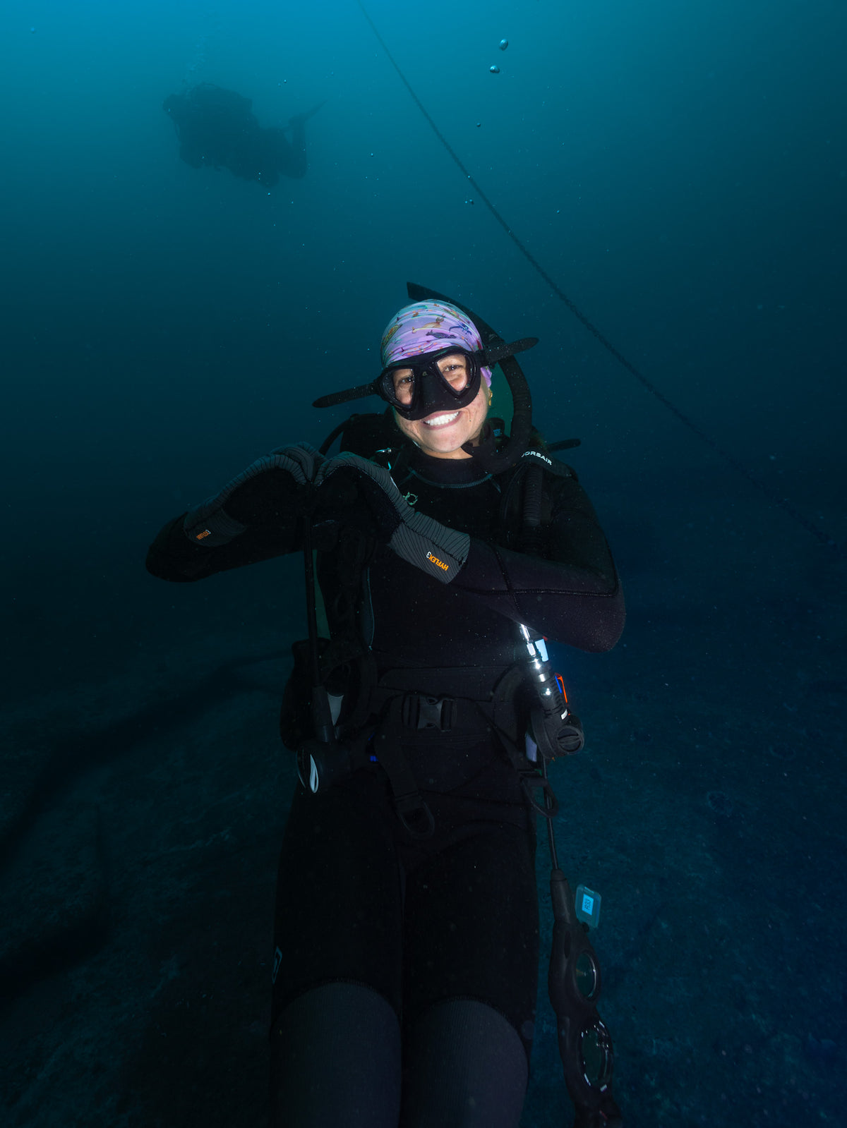 Scuba diver shown smiling underwater wearing nudibranch pink UV gaiter buff design made from recycled polyester-spandex ocean illustration by Diver Mon Art