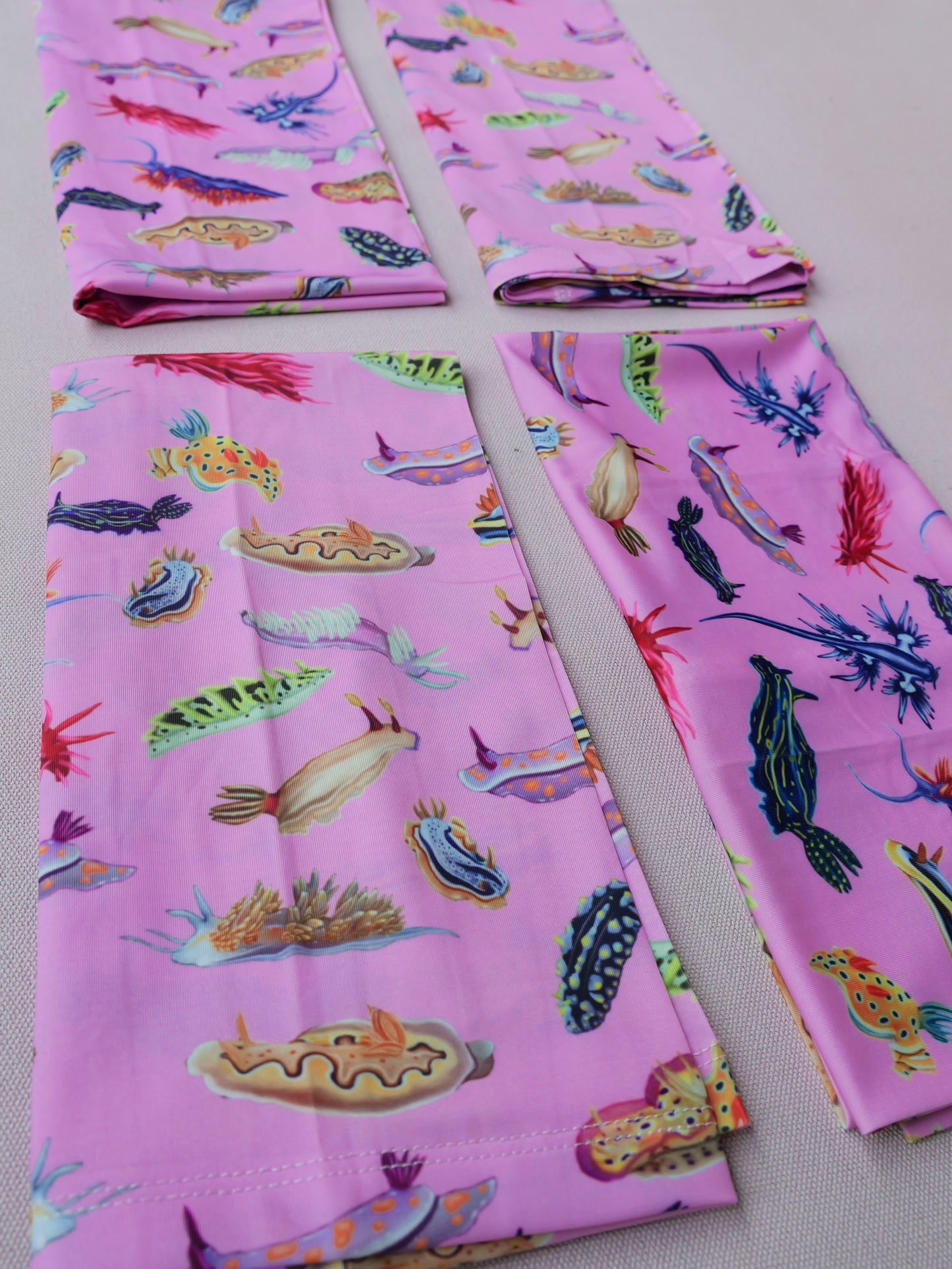 Four nudibranch pink UV gaiter buff design shown folded close up in great detail made from recycled polyester-spandex ocean illustration by Diver Mon Art