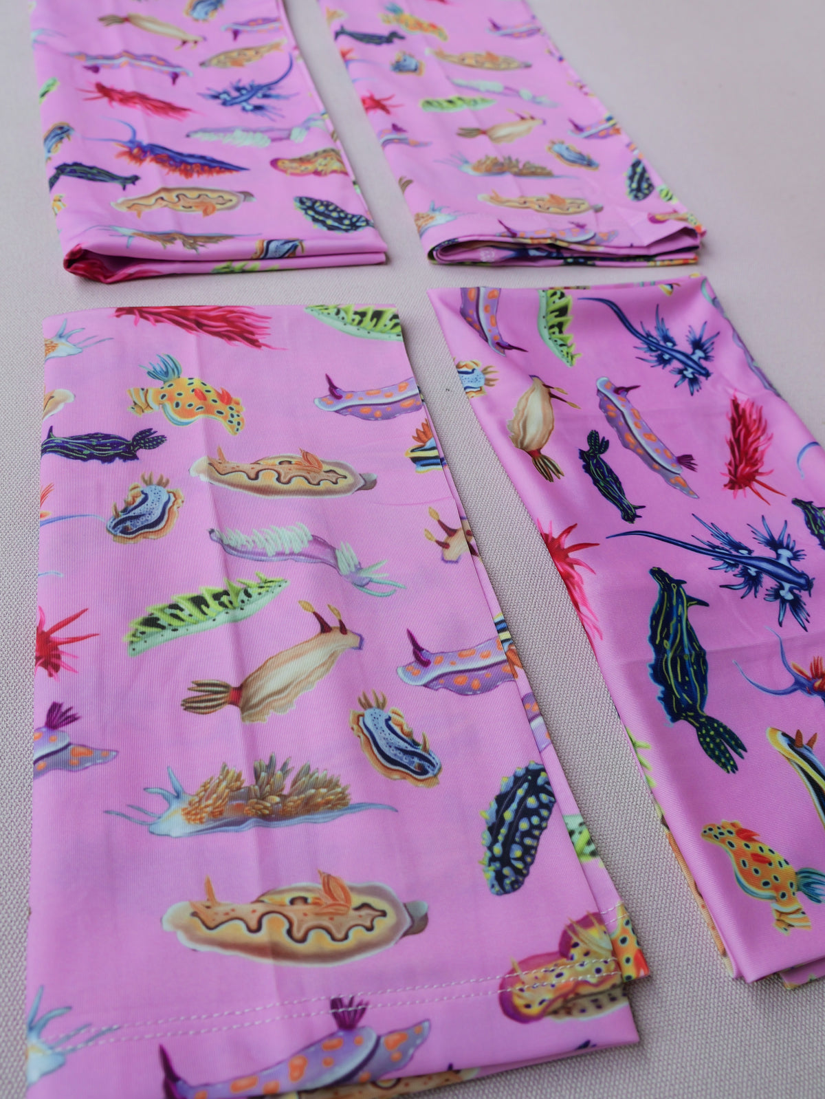 Four nudibranch pink UV gaiter buff design shown folded close up in great detail made from recycled polyester-spandex ocean illustration by Diver Mon Art