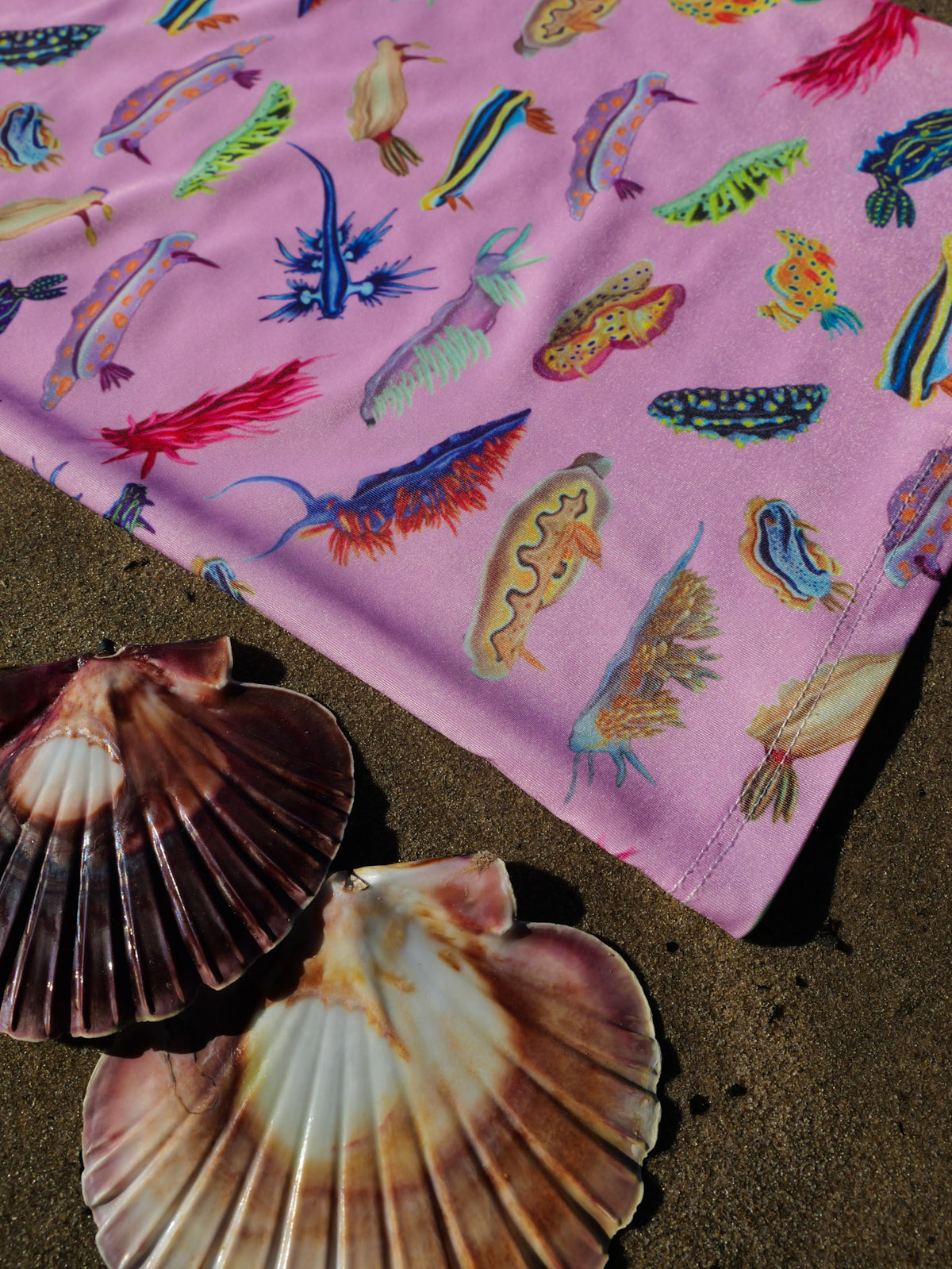 Nudibranch pink UV gaiter buff design shown bottom left corner close up in great detail sand shells background made from recycled polyester-spandex ocean illustration by Diver Mon Art