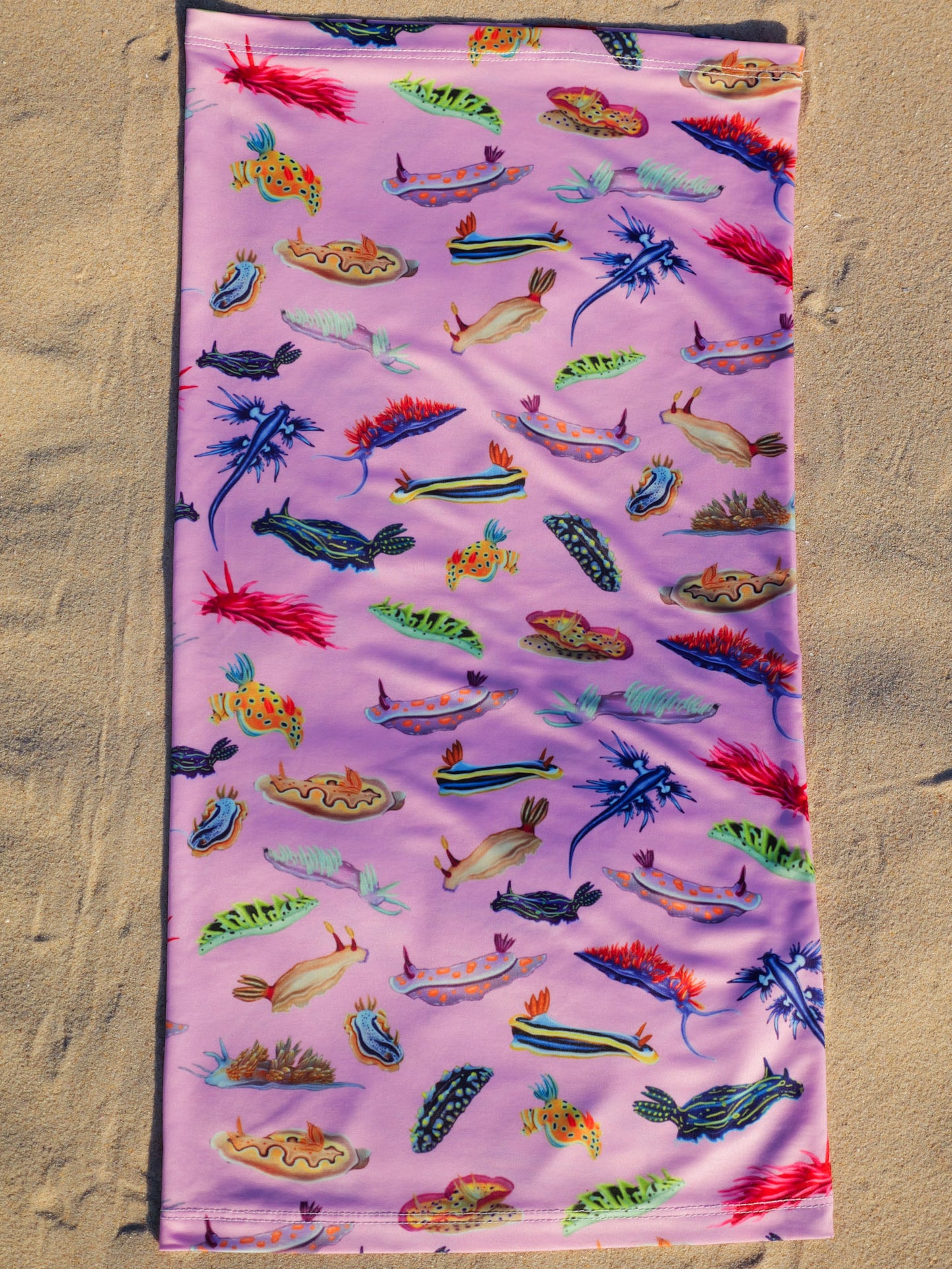 Nudibranch pink UV gaiter buff design shown laid out full length close up in great detail sand background made from recycled polyester-spandex ocean illustration by Diver Mon Art