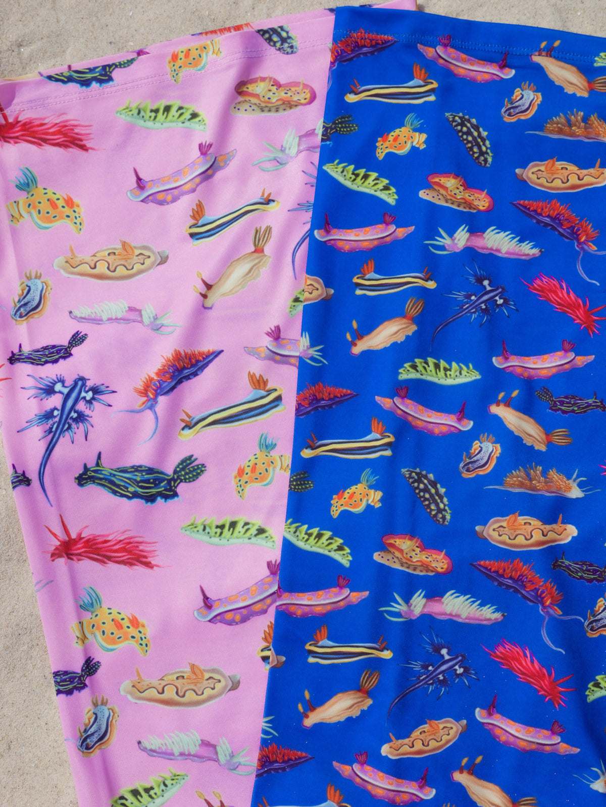 Nudibranch pink and dark blue UV gaiter buff design shown laid out full length close up in great detail sand background made from recycled polyester-spandex ocean illustration by Diver Mon Art
