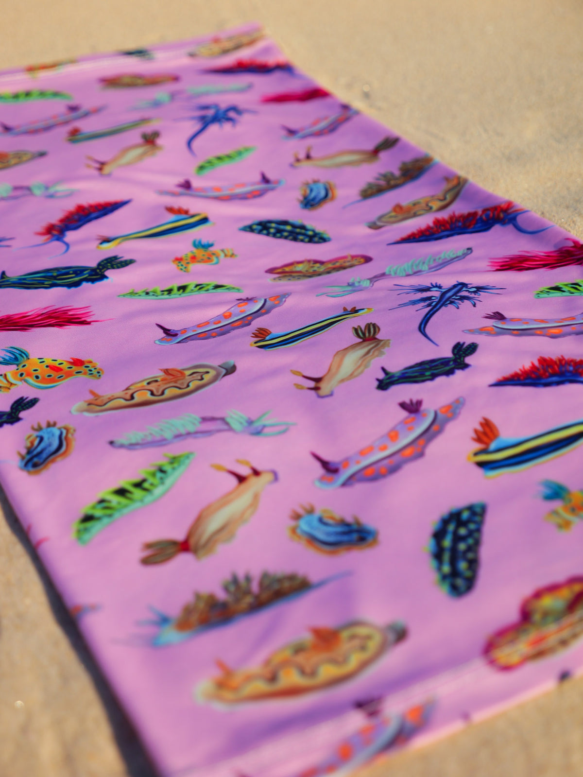 Nudibranch pink UV gaiter buff design shown laid out close up in great detail sand background made from recycled polyester-spandex ocean illustration by Diver Mon Art