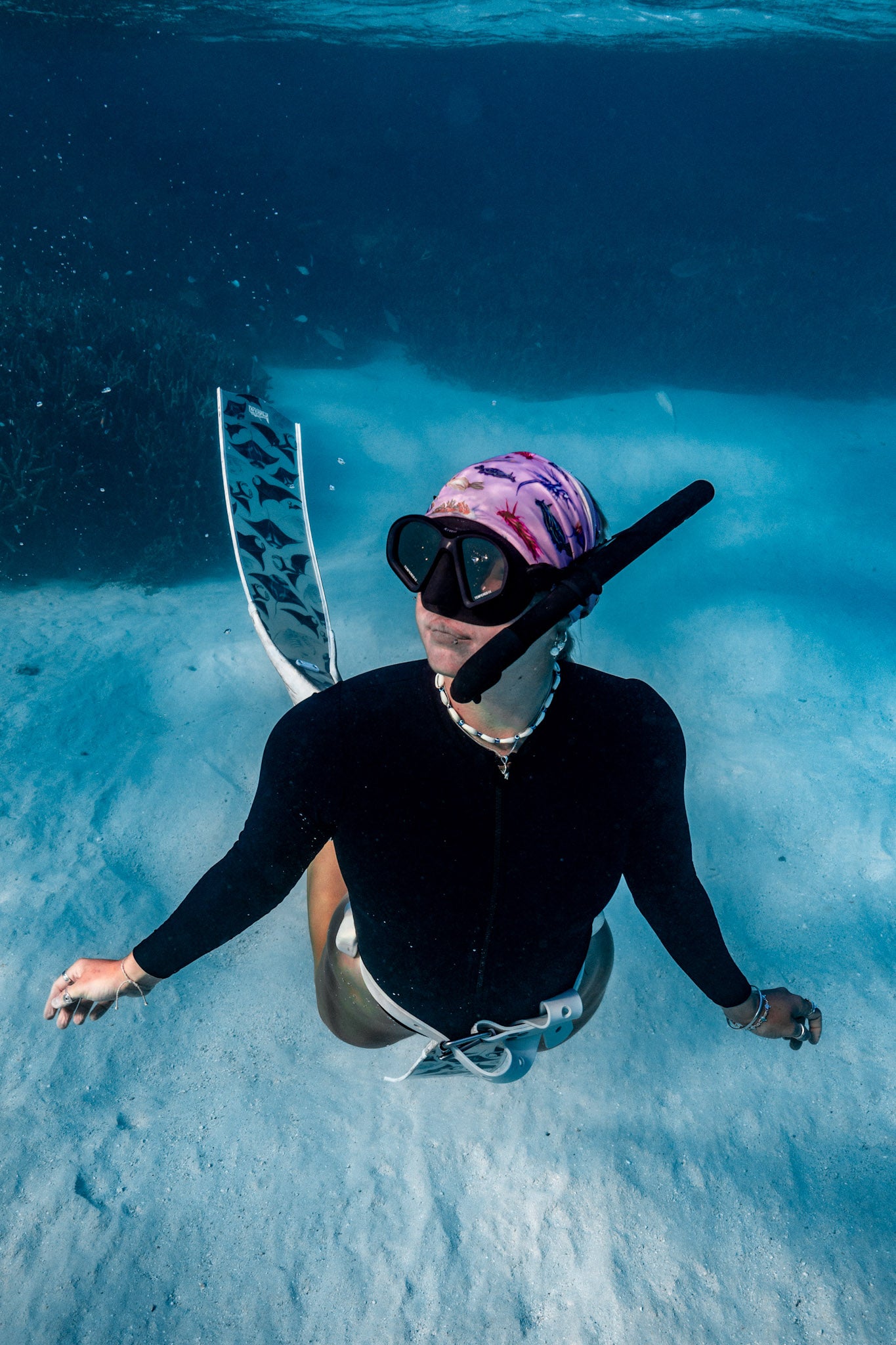Blonde haired women shown underwater clear blue water wearing nudibranch pink UV gaiter buff design made from recycled polyester-spandex ocean illustration by Diver Mon Art