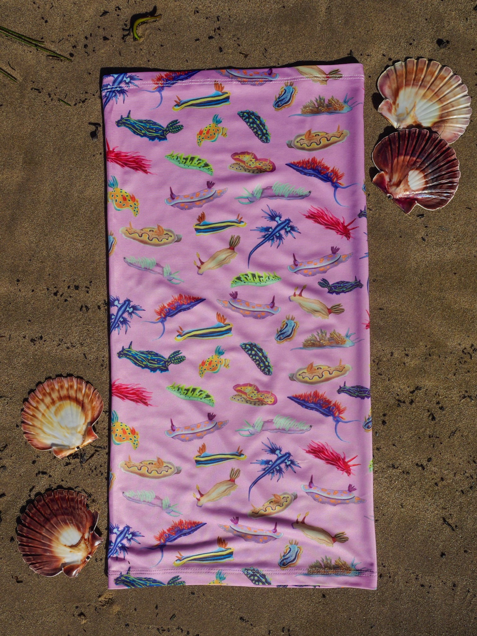 Nudibranch pink UV gaiter buff design shown laid out full length close up in great detail shells sand background made from recycled polyester-spandex ocean illustration by Diver Mon Art