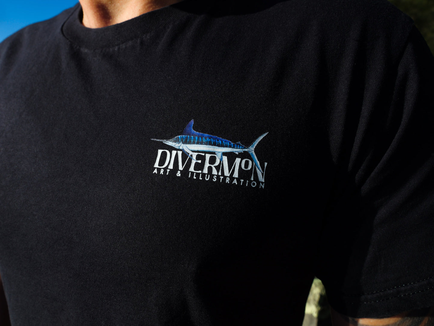 Black t-shirt with Diver Mon Art logo and marlin illustration on a person wearing it.