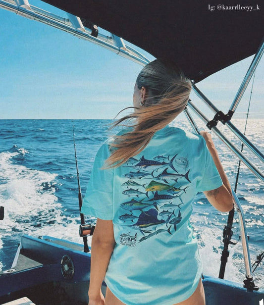 Woman on a boat wearing a light blue t-shirt with pelagic fish designs, looking out at the ocean.