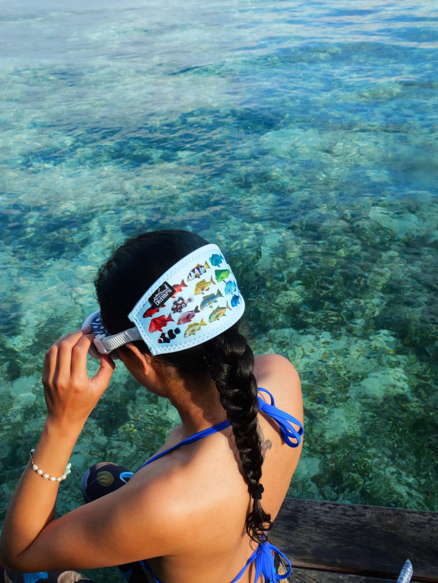 Dark haired woman seen from behind in clear blue water rainbow fish design with blue background neoprene mask strap tamer ocean illustration by Diver Mon Art 