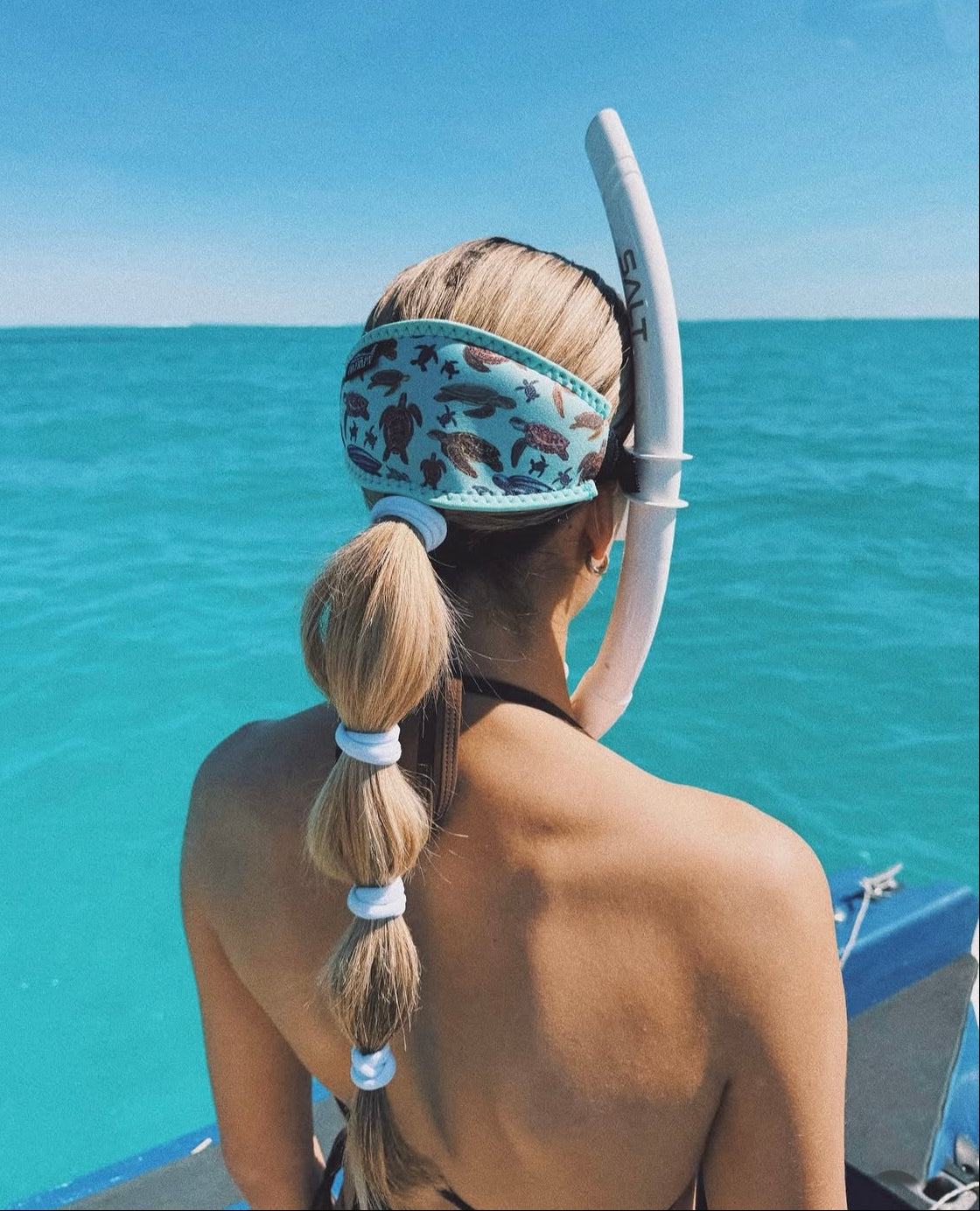 Blonde haired woman seen from close up behind in clear blue water sea turtles design with light green background neoprene mask strap tamer ocean illustration by Diver Mon Art 