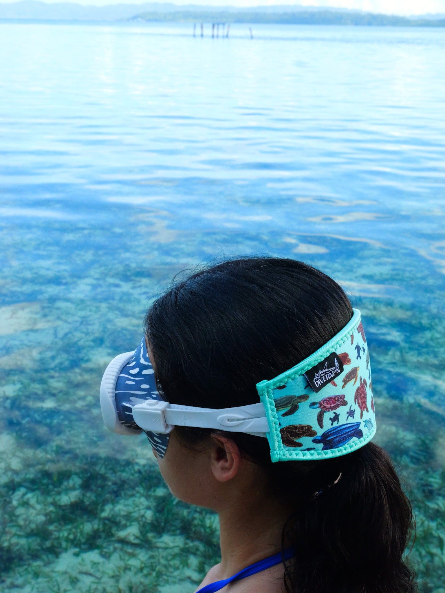 Dark haired woman shown from a side view in blue clear water close up green turtle design neoprene mask strap tamer ocean illustration by Diver Mon Art
