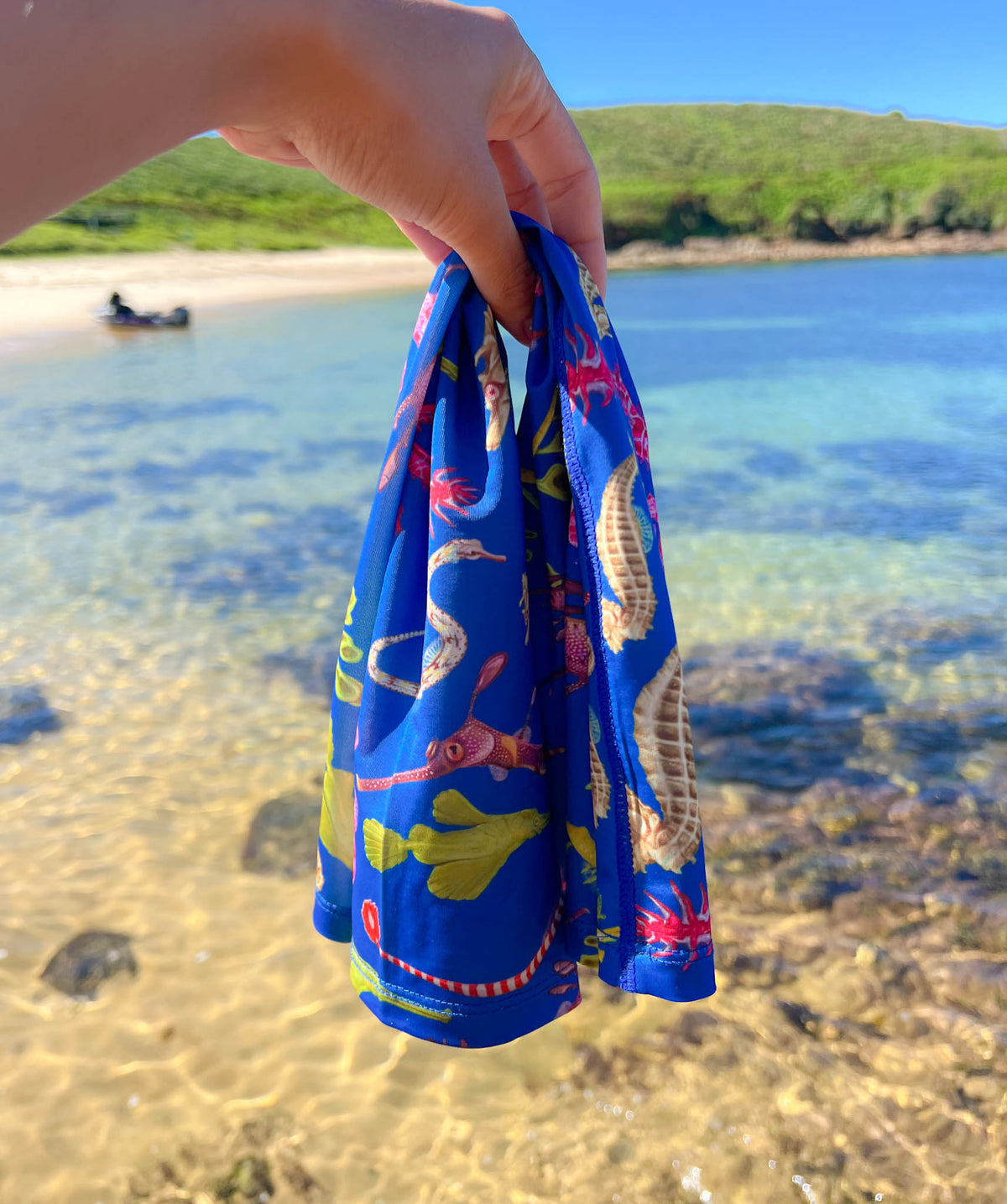 Seahorse dark blue UV gaiter buff design shown held out by hand by the clear waters edge close up in great detail made from recycled polyester-spandex ocean illustration by Diver Mon Art
