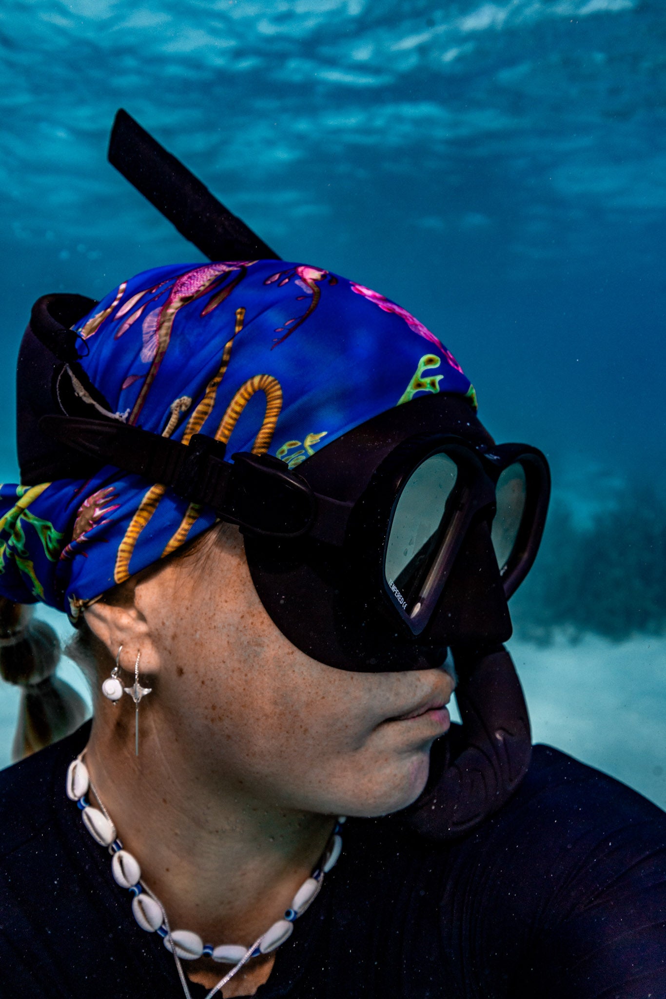 Blonde haired women shown close up great detail underwater clear blue water wearing seahorse dark blue UV gaiter buff design made from recycled polyester-spandex ocean illustration by Diver Mon Art