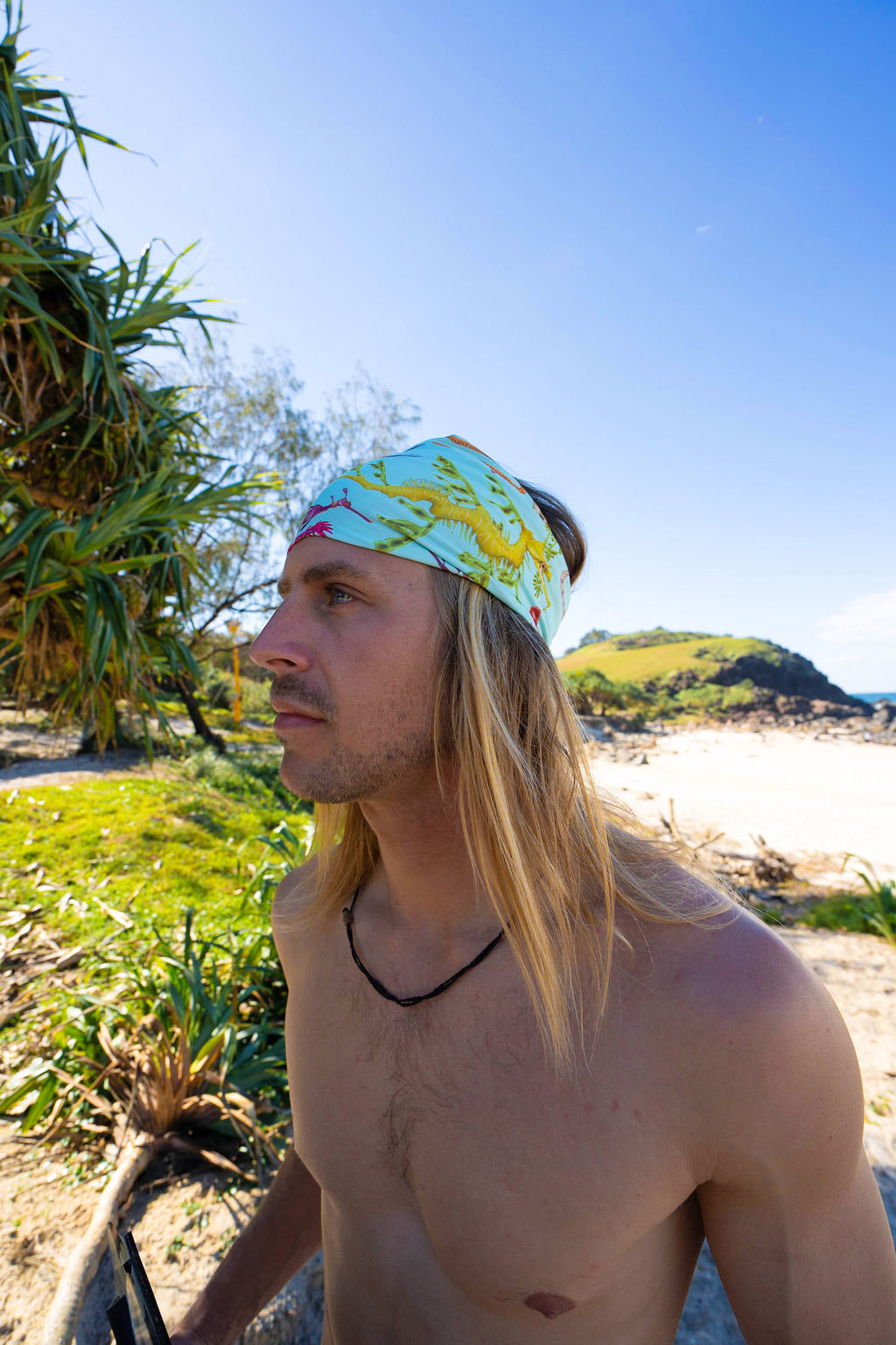 Man shown close up at the beach in the shade wearing the seahorse green UV gaiter buff design made from recycled polyester-spandex  in a headband way ocean illustration made by Diver Mon Art