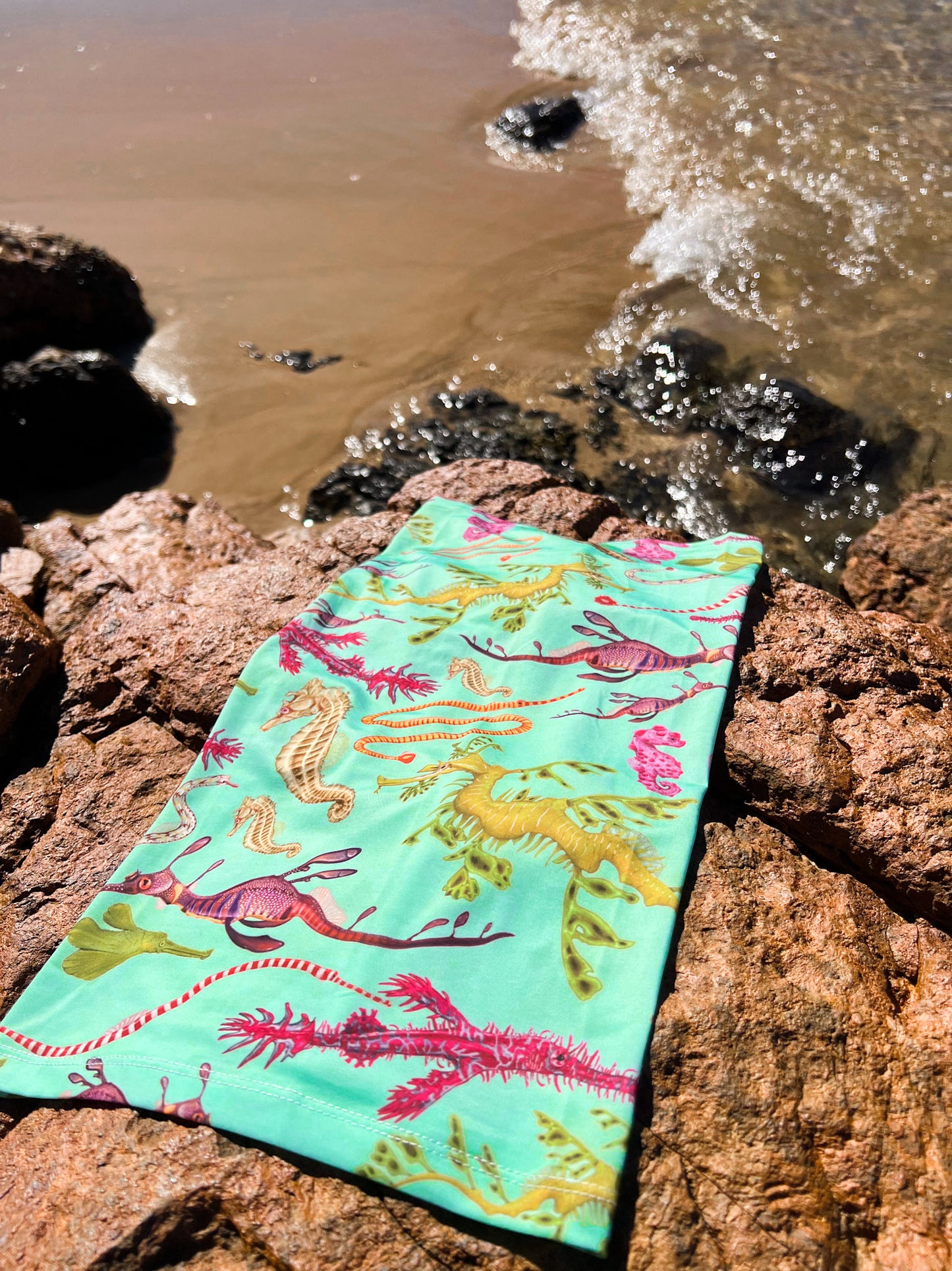 Seahorse green UV gaiter buff design shown laid out on a rock by the waters edge close up in great detail made from recycled polyester-spandex ocean illustration by Diver Mon Art