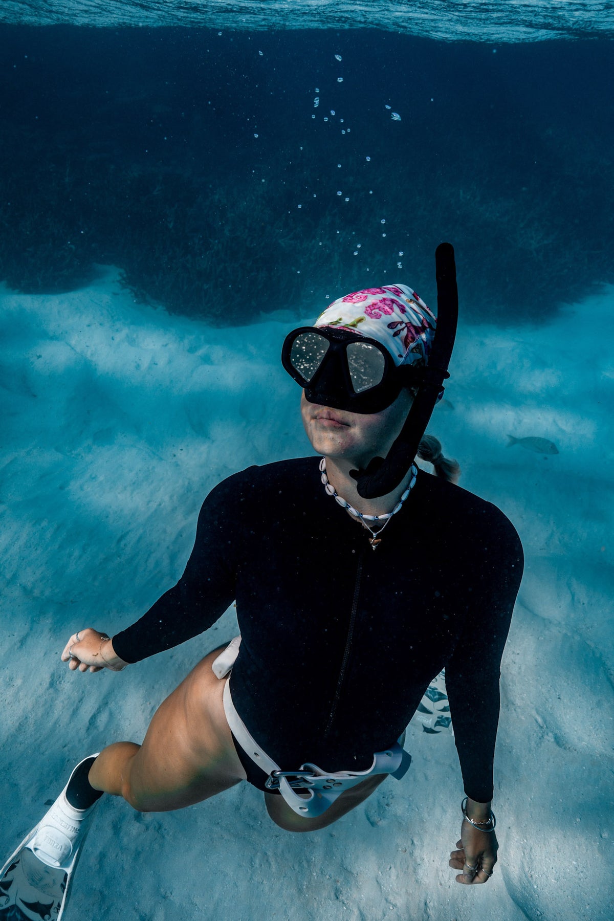 Blonde haired women shown underwater clear blue water wearing seahorse green UV gaiter buff design manta white fins made from recycled polyester-spandex ocean illustration by Diver Mon Art